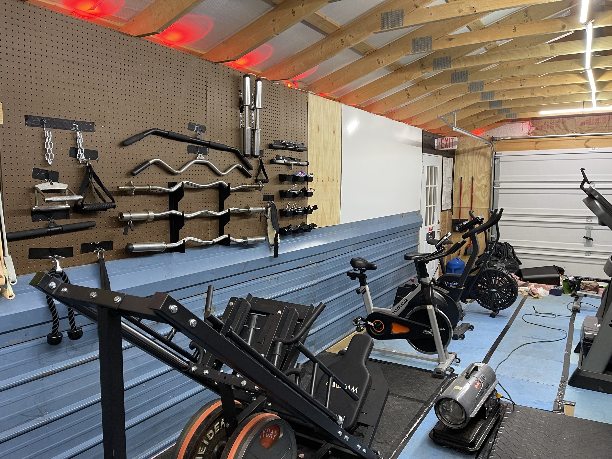 Home gym with exercise equipment including bikes, weights, and a treadmill, with a pegboard wall for workout tools and a blue floor.