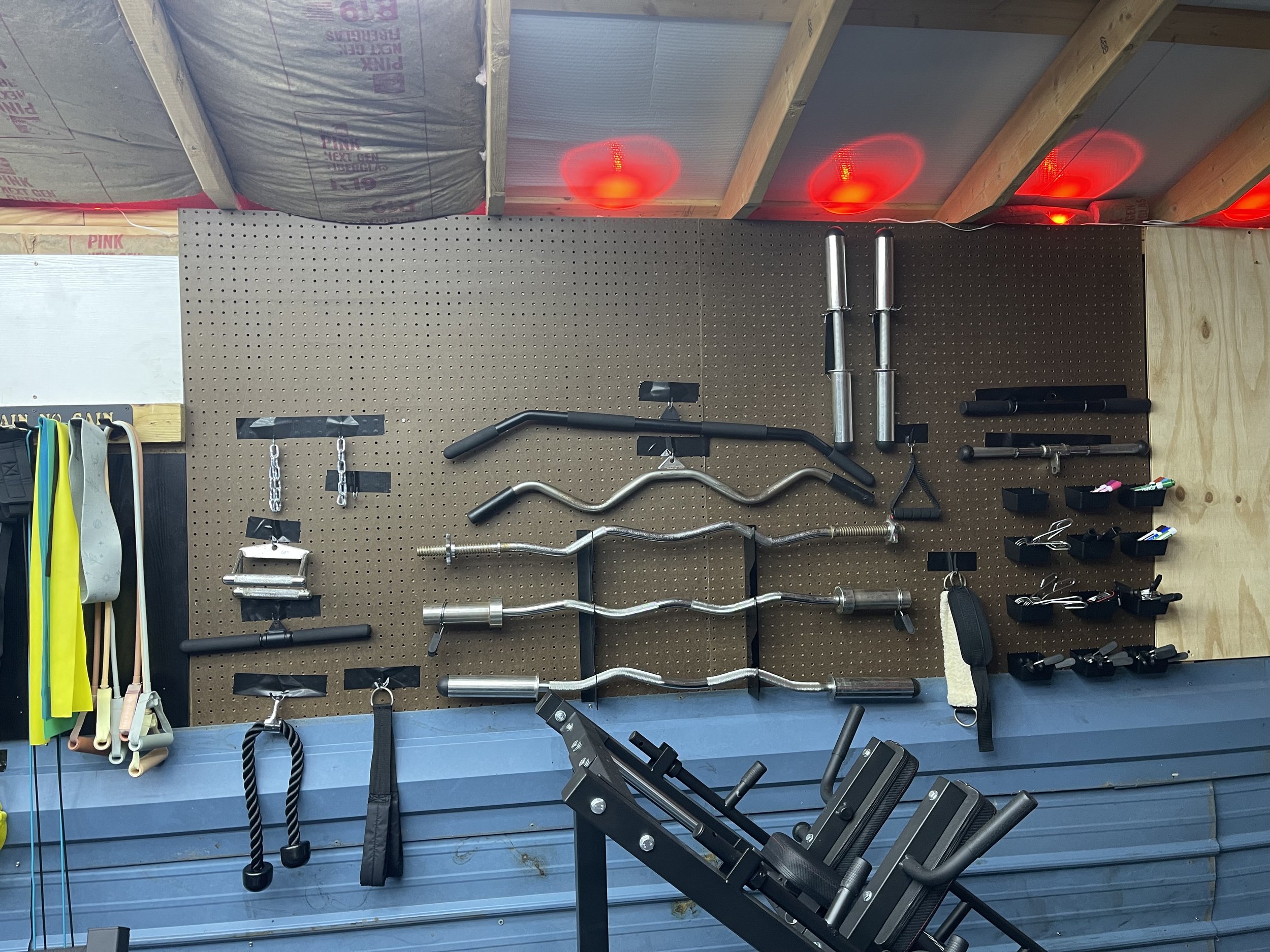 Workout equipment including barbells, resistance bands, weight plates, and small accessories organized on a pegboard in a gym.