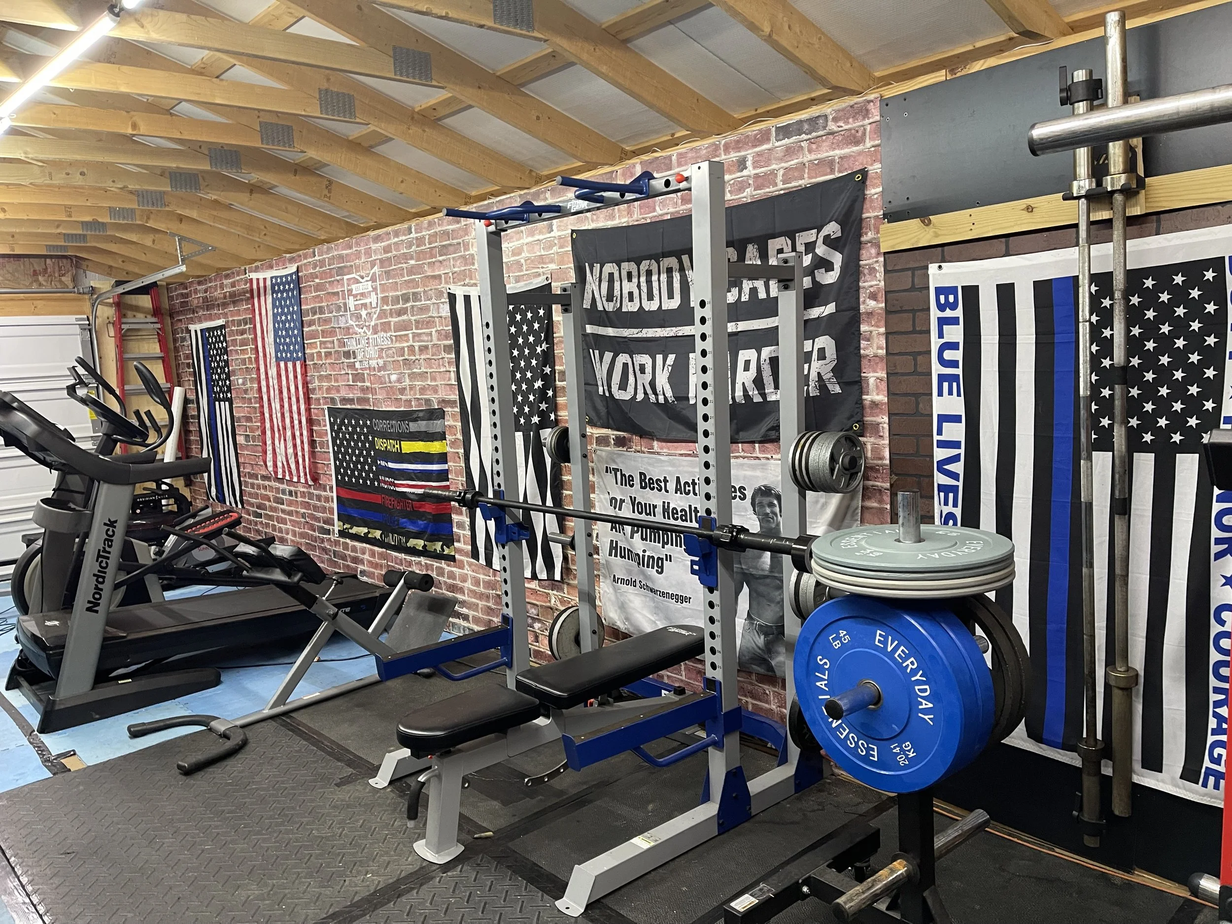 Home gym with treadmill, weightlifting equipment, and flags on brick wall