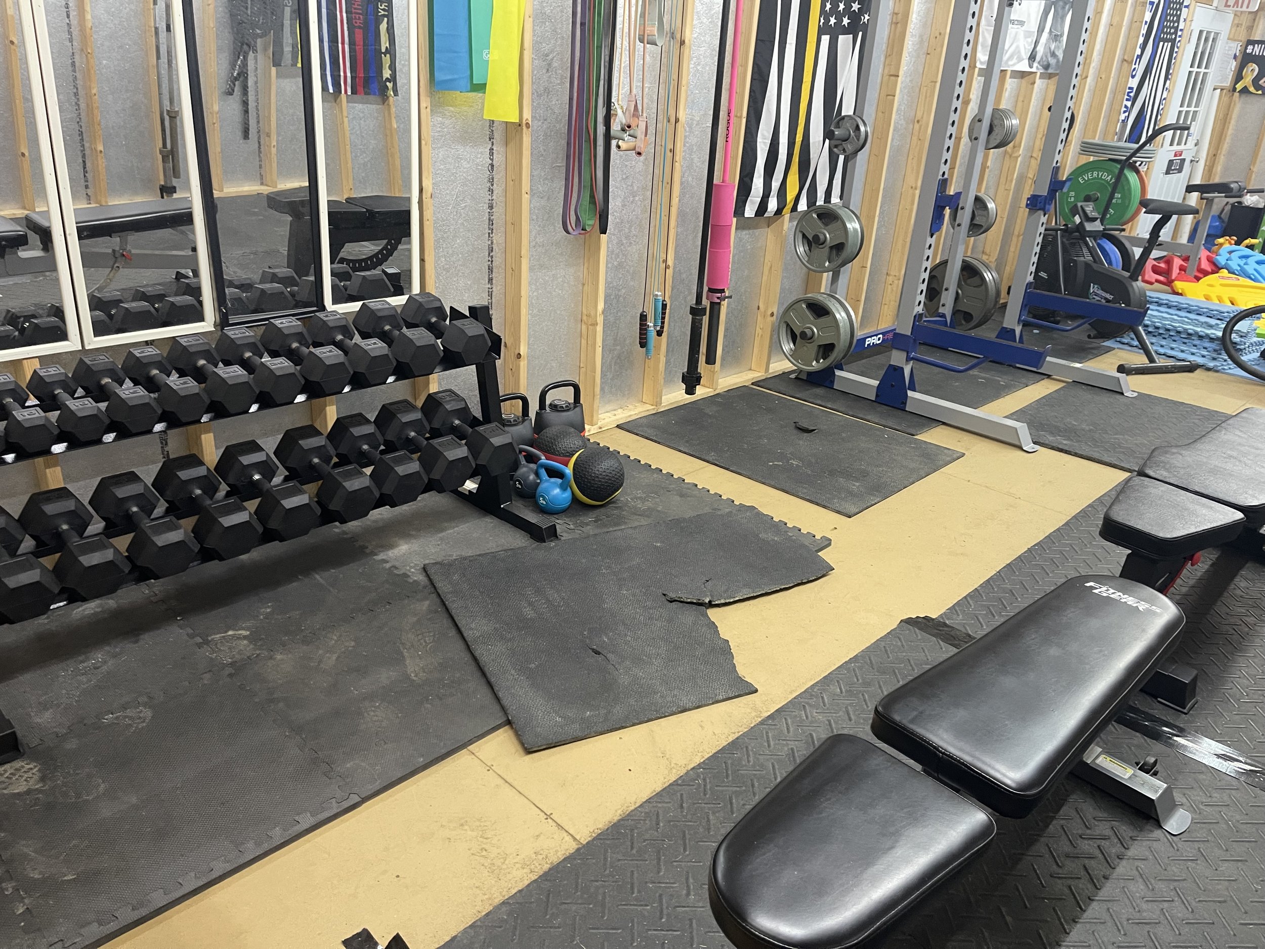 A home gym with dumbbells, kettlebells, medicine balls, resistance bands, and weightlifting equipment, including a bench and weight racks.