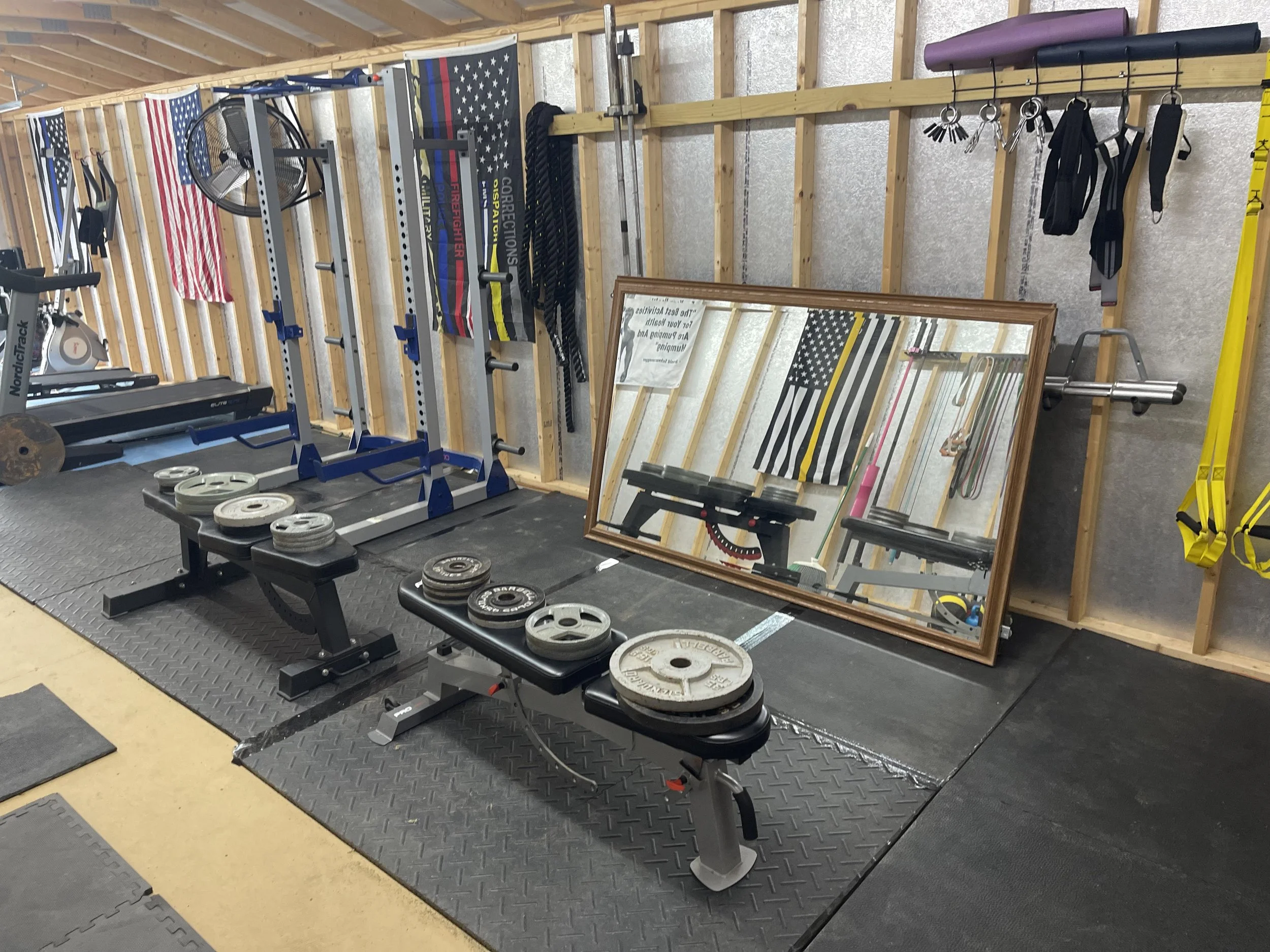 A home gym with workout equipment including weights, a mirror, kettlebells, and flags on the wall.
