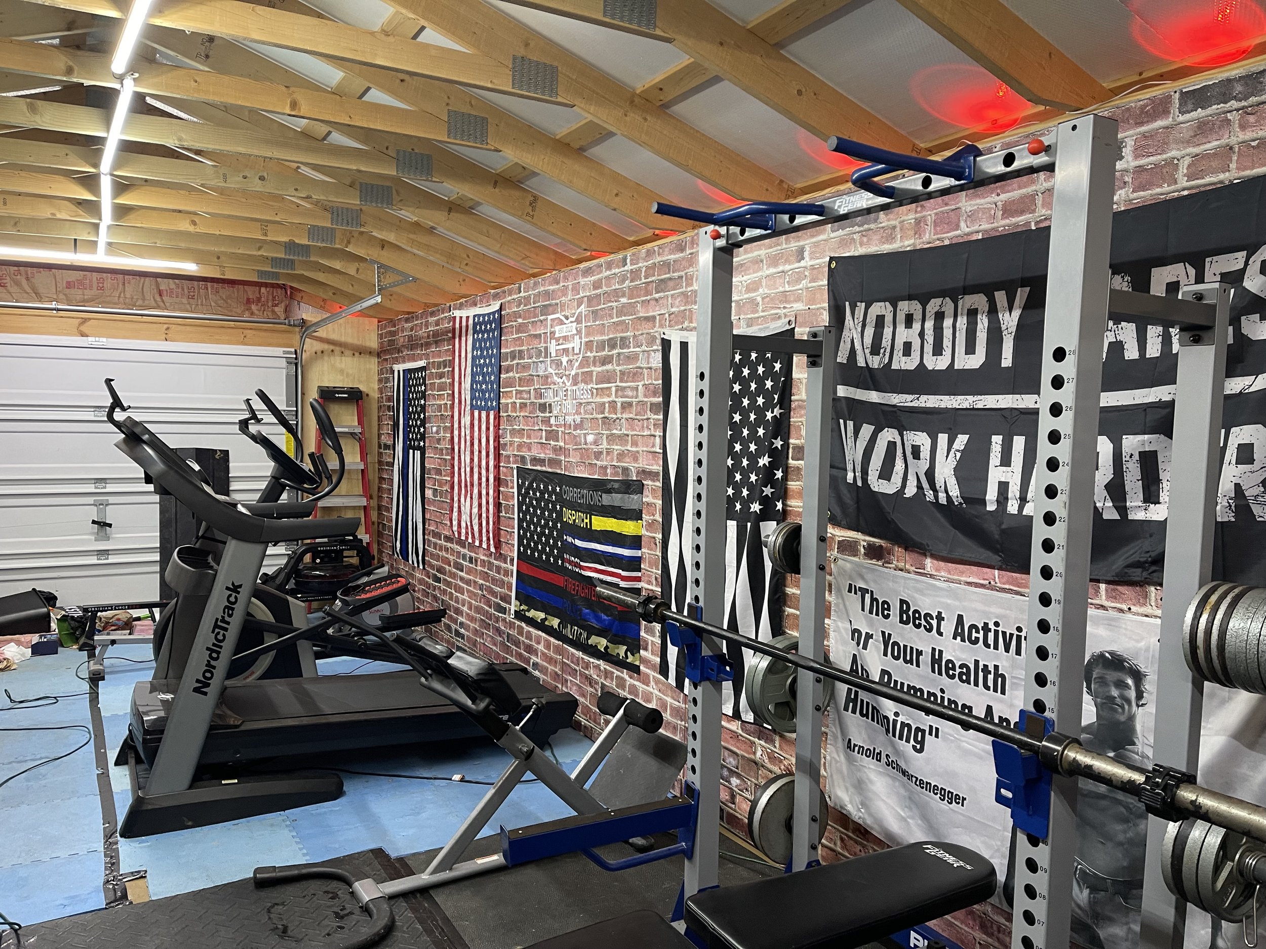 Home gym with treadmills, weightlifting equipment, and motivational banners on brick wall.