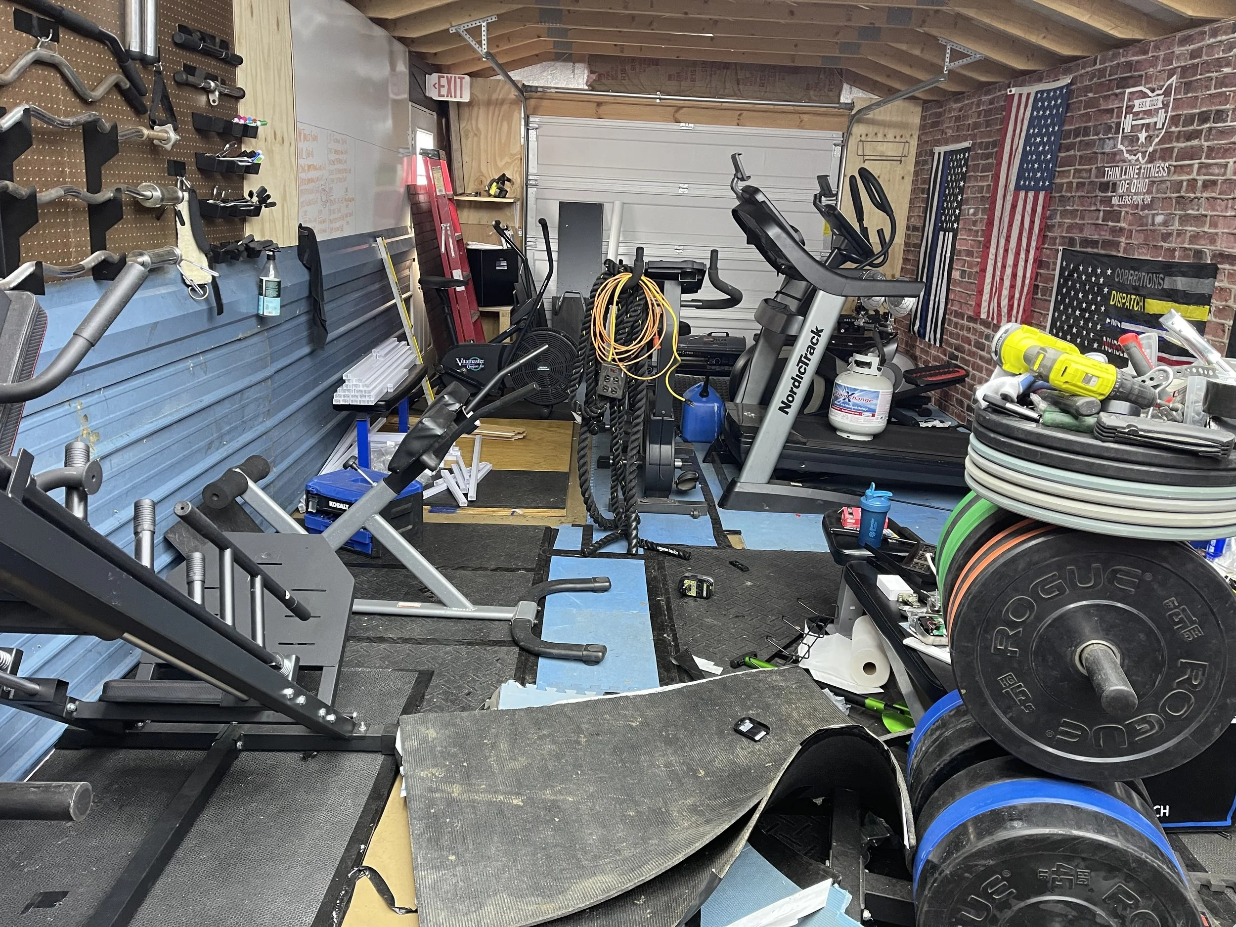 Home gym with workout equipment, weights, treadmill, exercise bike, wall-mounted tools, and American flags.