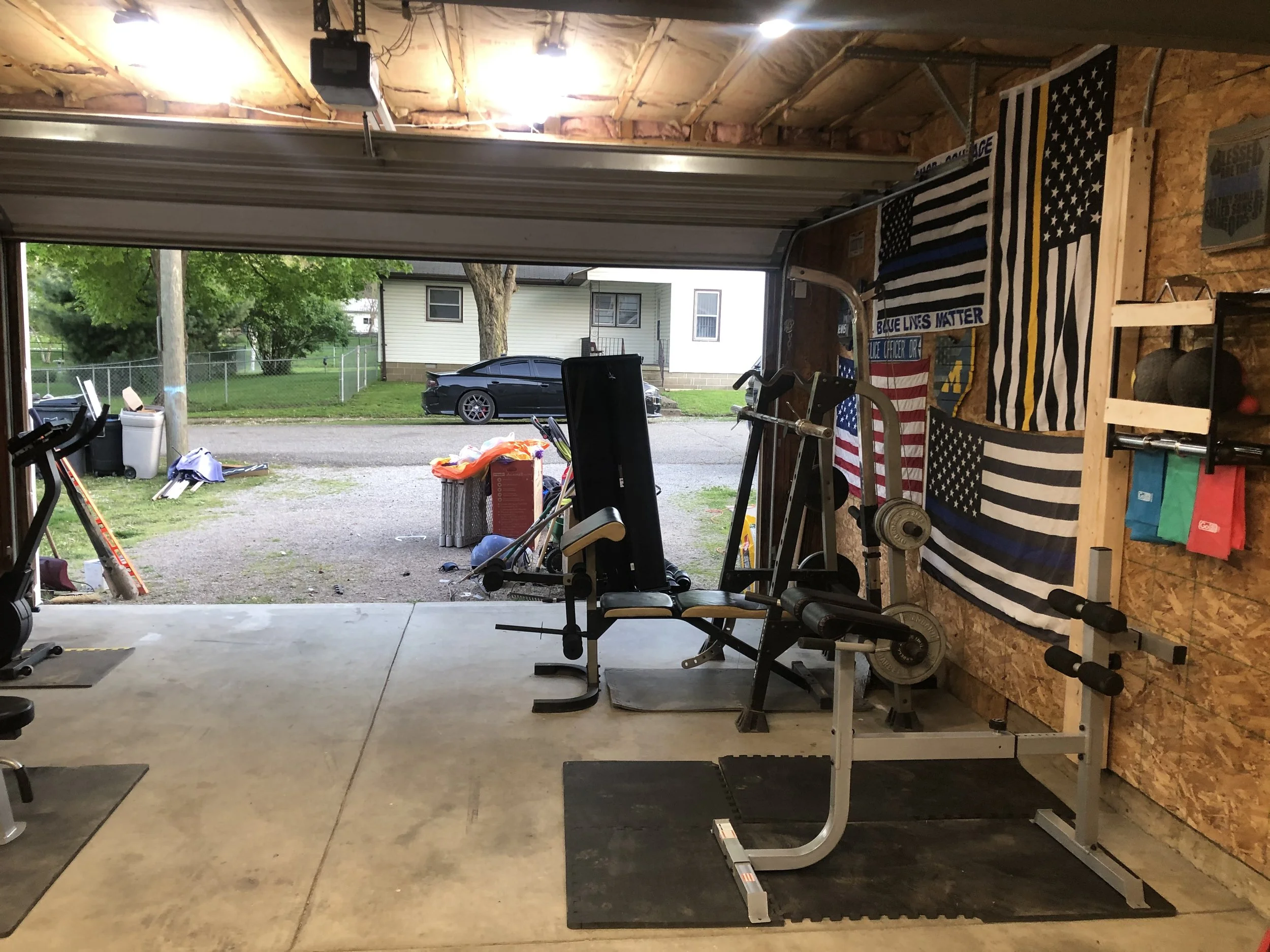 View of a garage with workout equipment, American flags, and a view outside of a street with a black car parked.