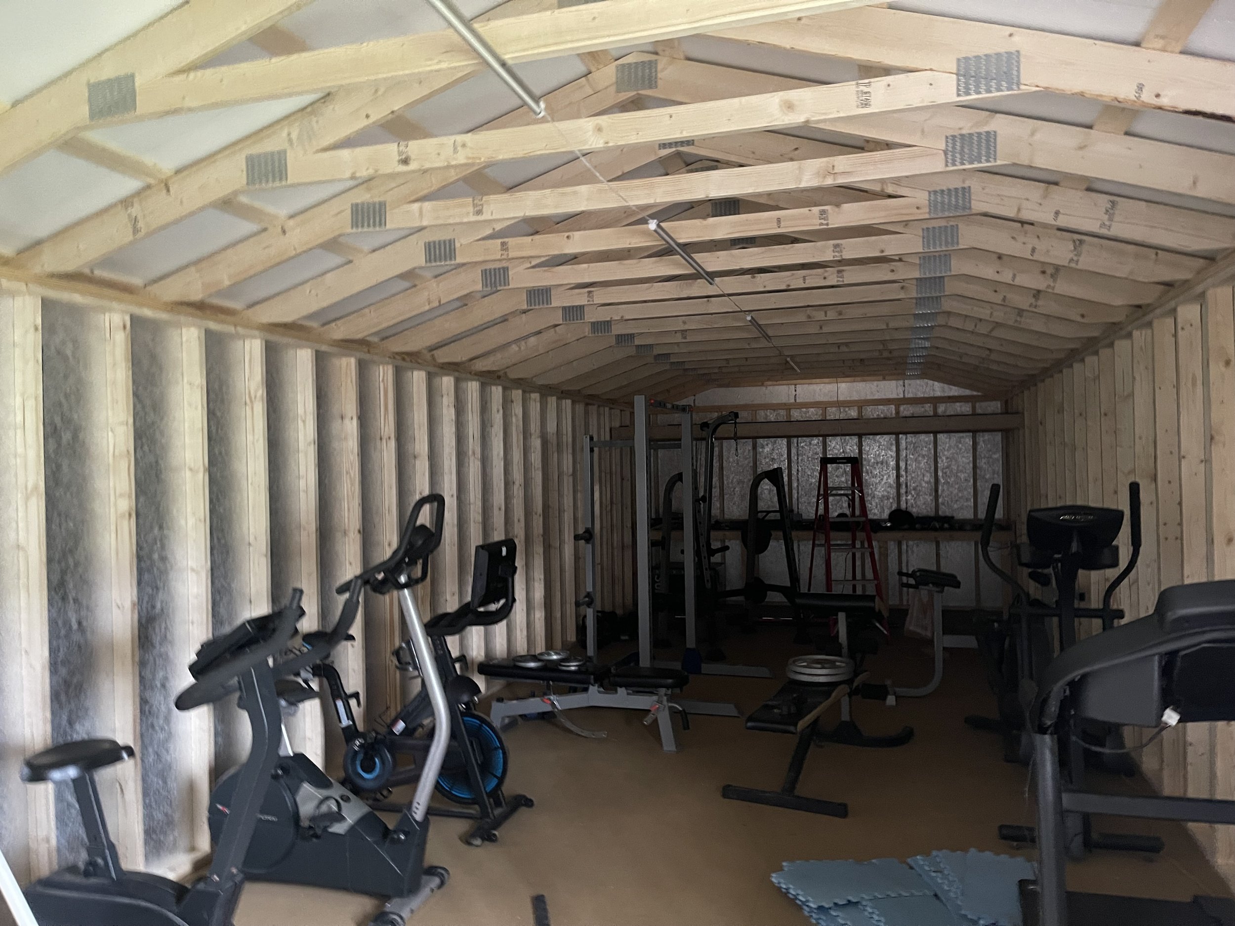 Home gym in a partially finished attic with exercise bikes, weightlifting equipment, and foam mats.