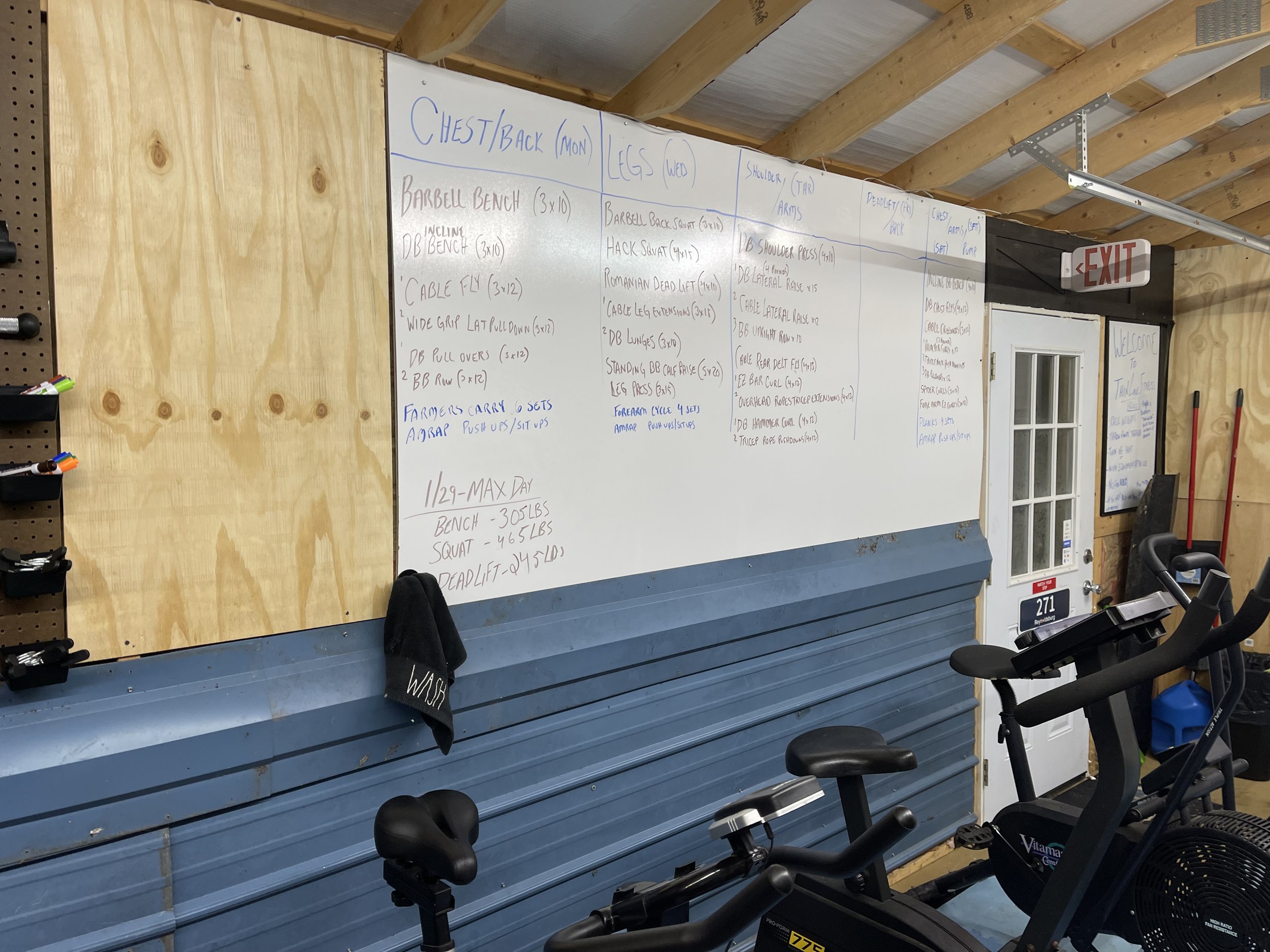Gym training whiteboard with workout routines and schedules, exercise bikes, and workout equipment in the background.