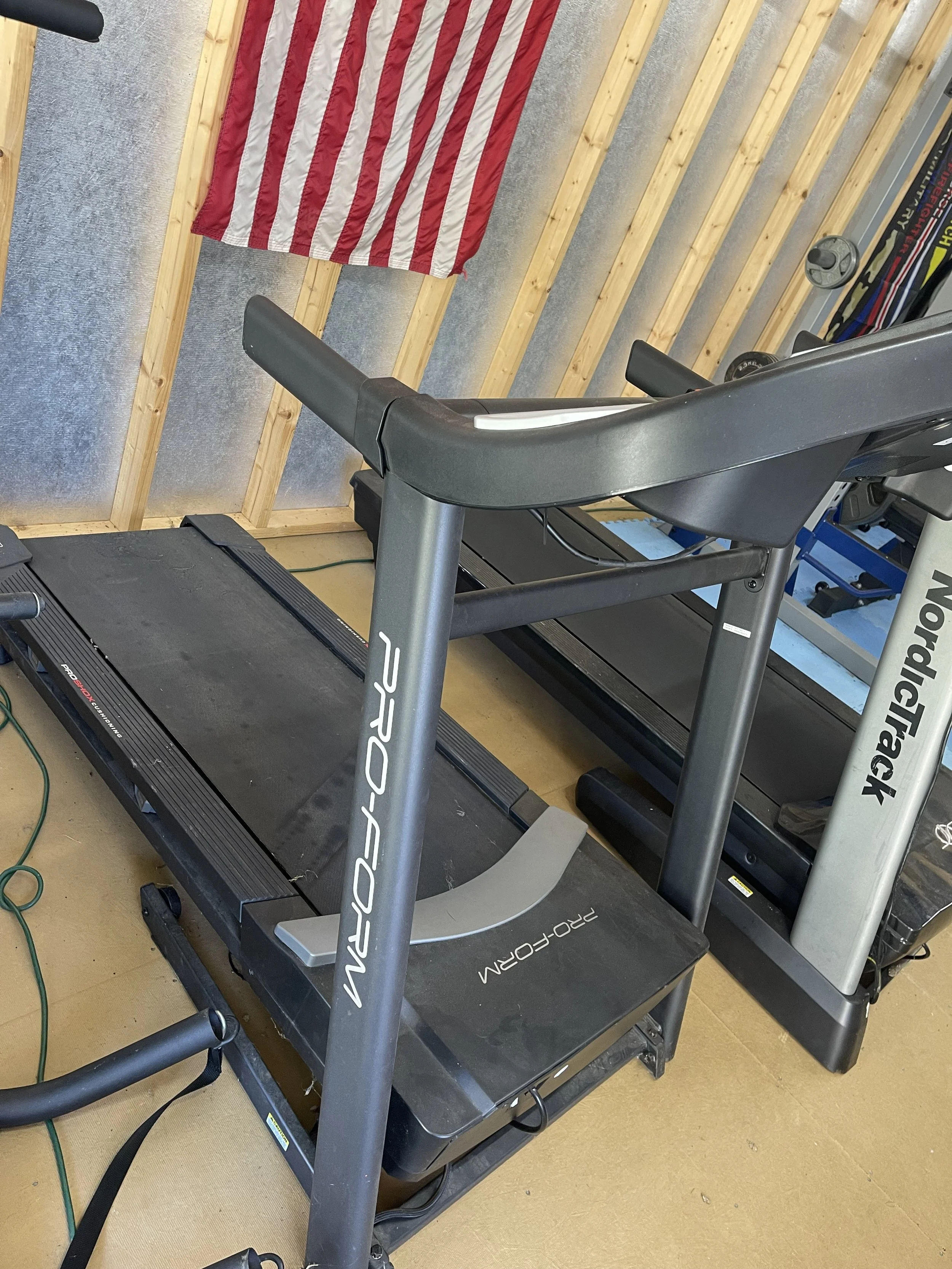 A ProForm treadmill in a garage gym with an American flag on the wall.