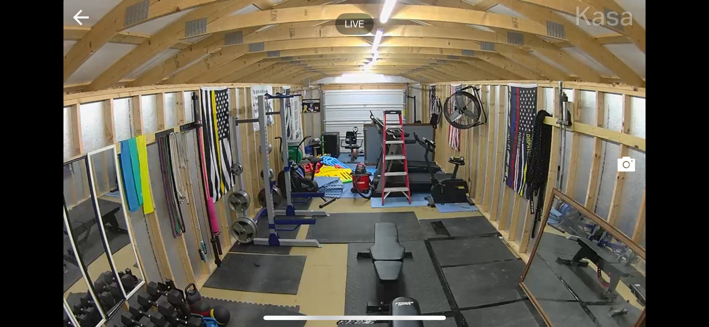 An organized home gym with wooden framing, various workout equipment, weights, resistance bands, a mirror, and a treadmill.