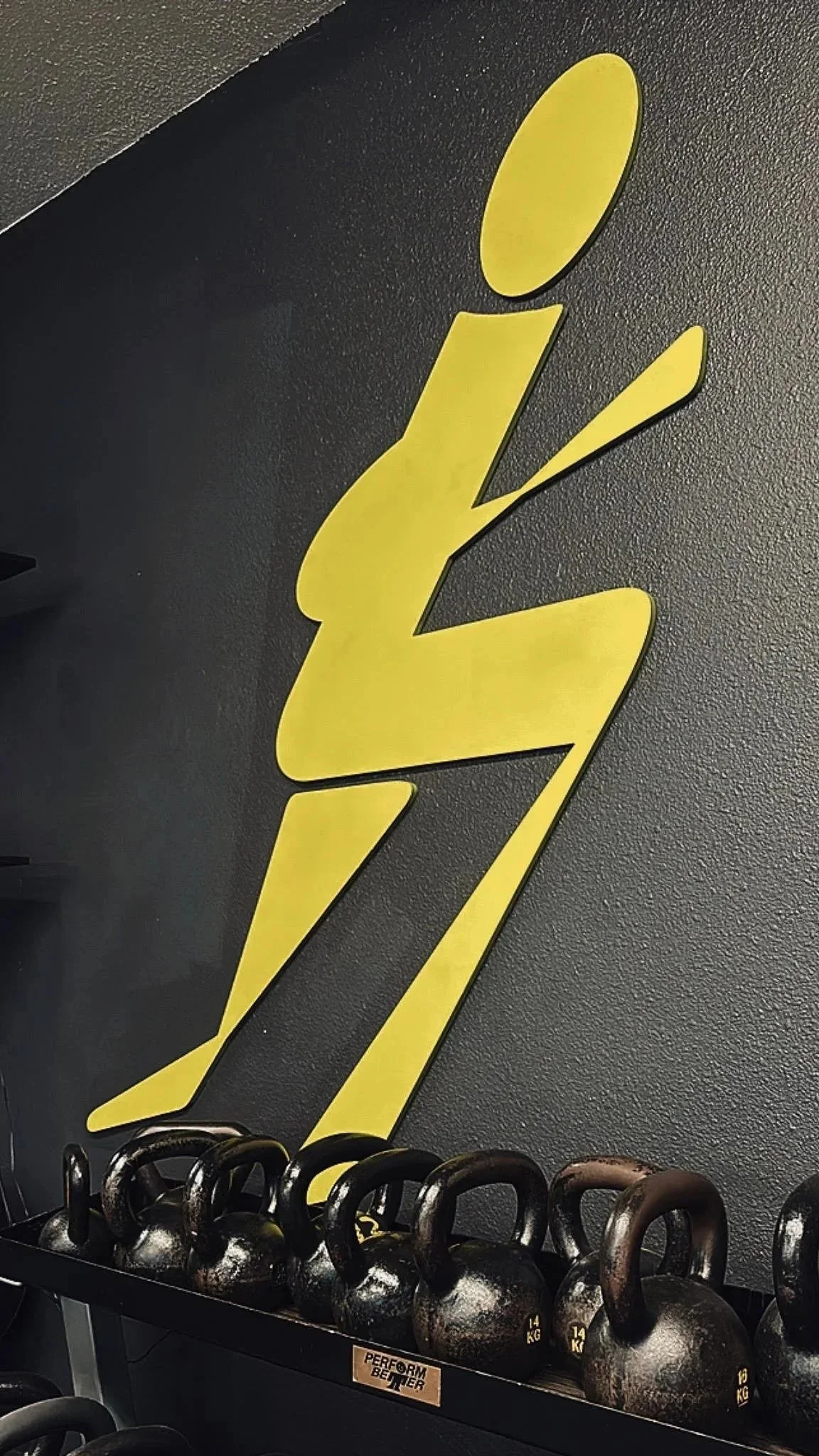 Yellow stylized letter 'Z' logo on a dark wall, with kettlebells and black rubber flooring in a gym setting.