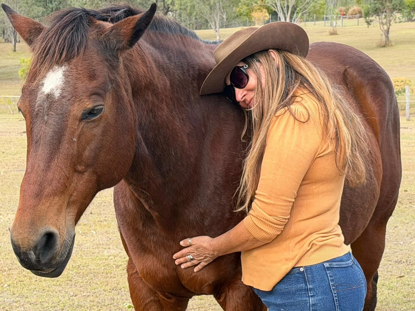 A woman hugging a brown horse in a grassy outdoor setting.
