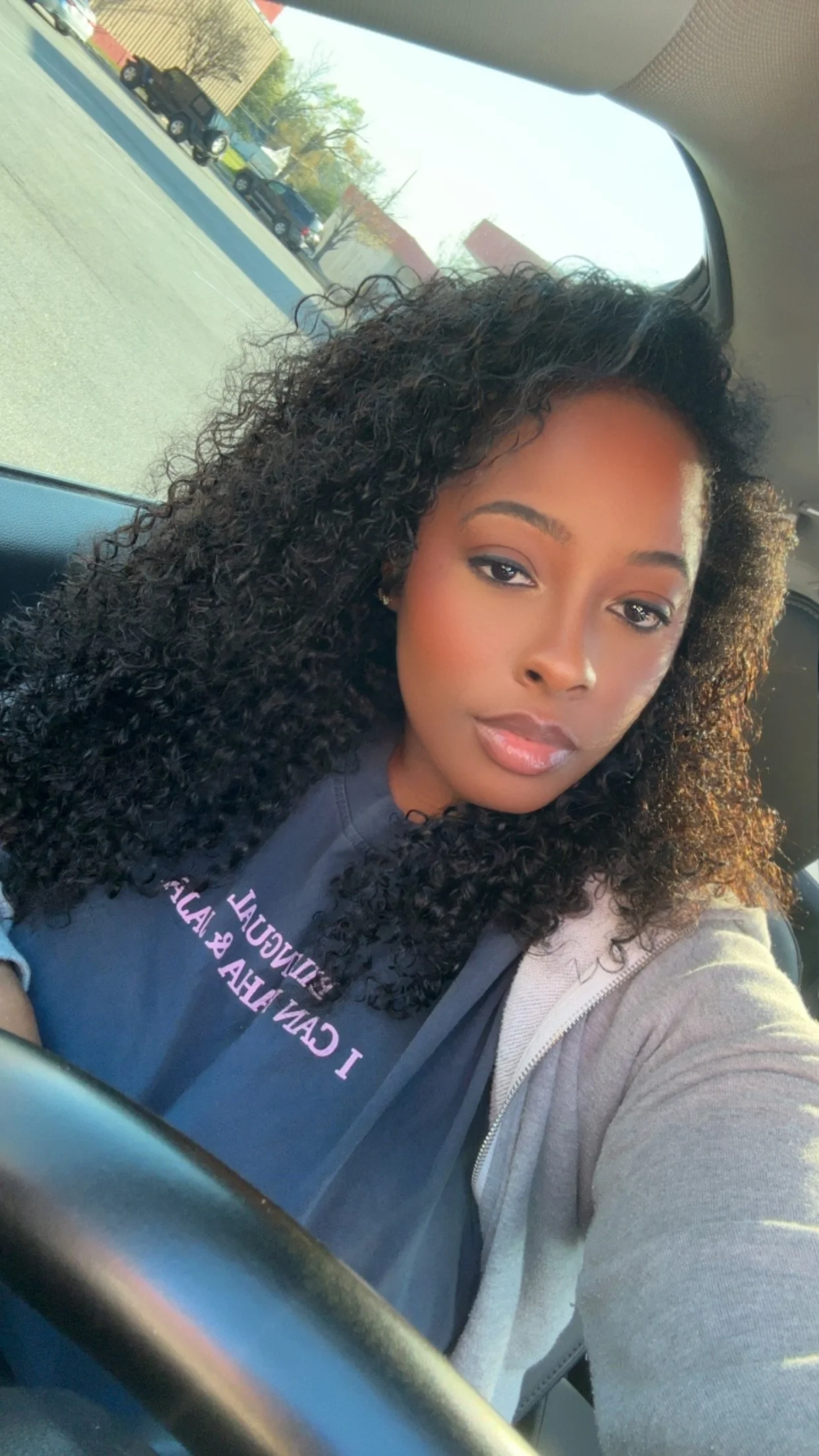 A woman with curly hair sitting in a car, taking a selfie.