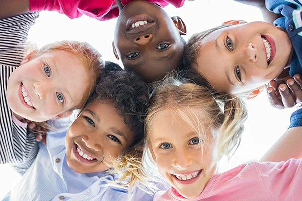 Children of diverse ethnicities smiling and looking down at the camera in a circular formation