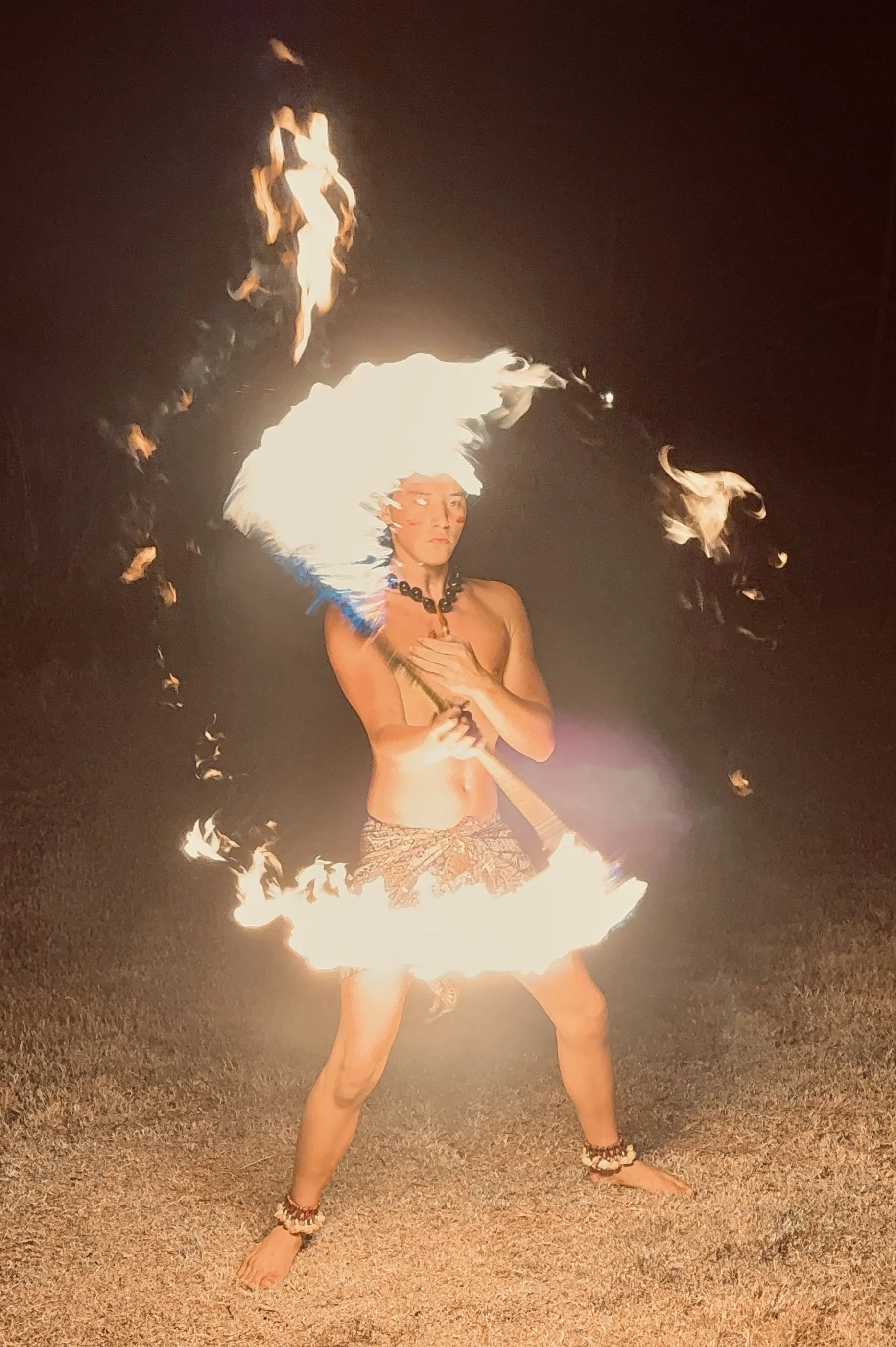 Kaneli performing fire dancing outdoors at night, wearing traditional tribal accessories and holding a Fire Knife.