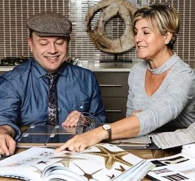 Adam Scougall and woman sitting at a table, smiling and looking at a tablet, with nature-themed books and decor in the background.