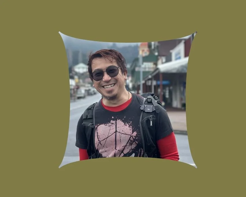 Smiling man with sunglasses, short hair, and a backpack on a city street.