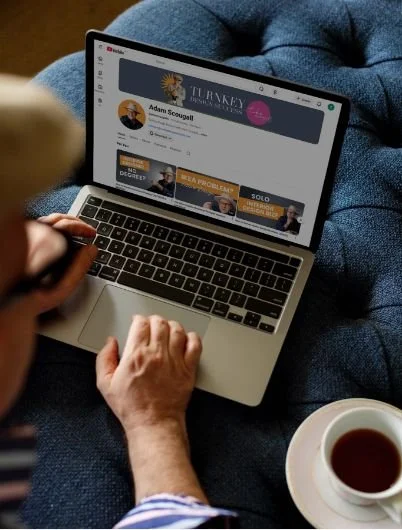 Person using a laptop with Adams YouTube Channel open, sitting on a blue couch with a cup of tea nearby.