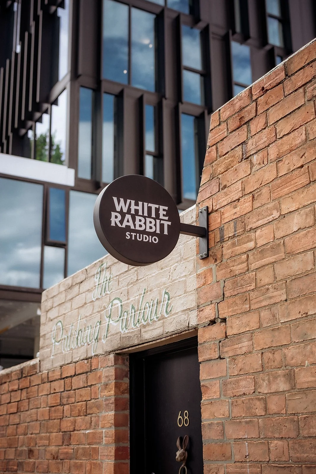 Exterior view of White Rabbit Studio sign mounted on a brick wall above a doorway, with modern building windows in the background