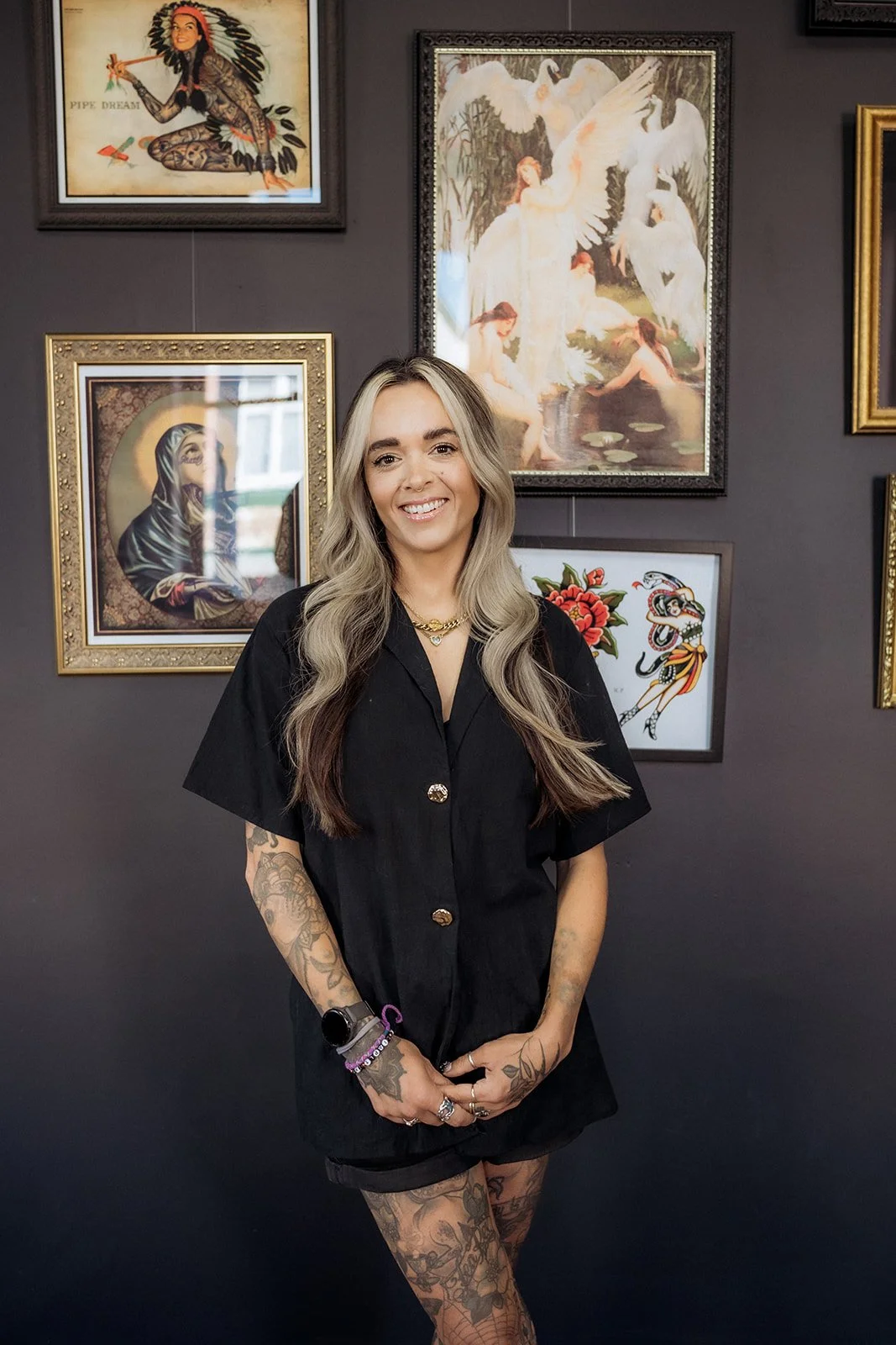 Smiling tattooed woman standing in studio against a gallery wall of framed artwork