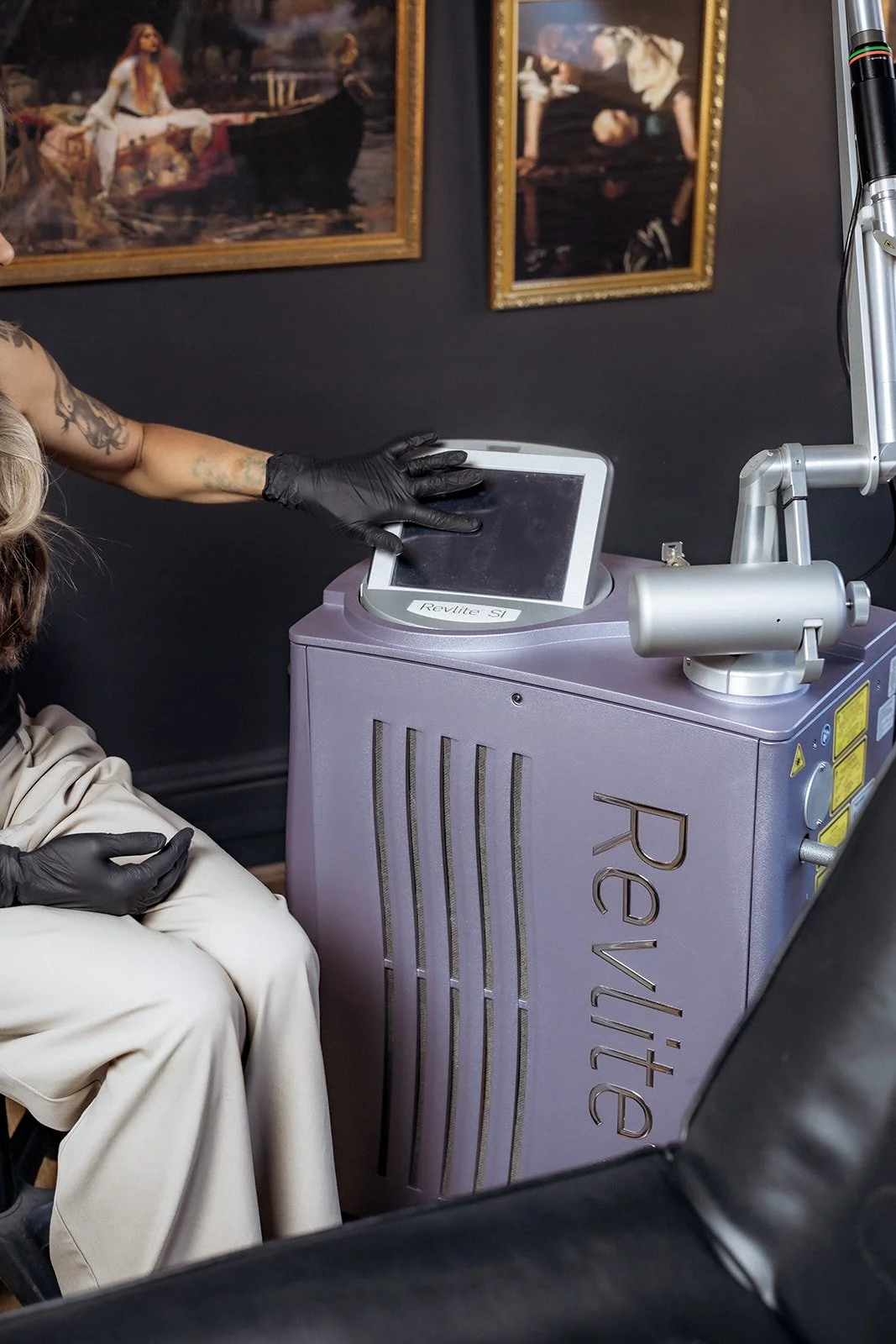 Technician operating RevLite SI laser machine used for tattoo removal inside studio setting