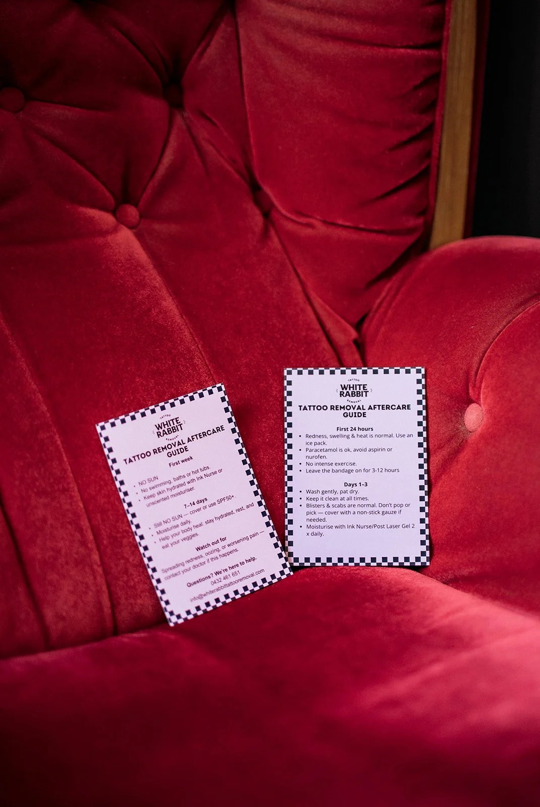 Two tattoo removal aftercare instruction cards resting on a plush red velvet chair, branded “White Rabbit” with care guidelines visible