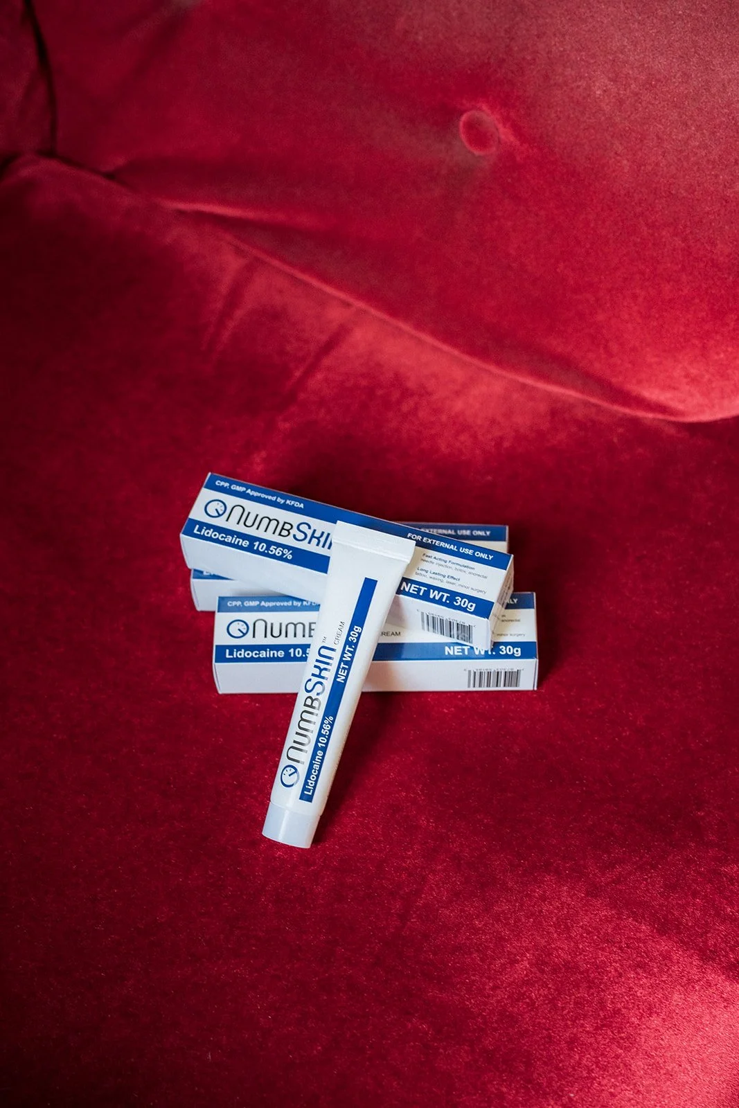 Tube and boxes of NumbSkin lidocaine numbing cream placed on a red velvet chair, used for pain management during tattoo procedures