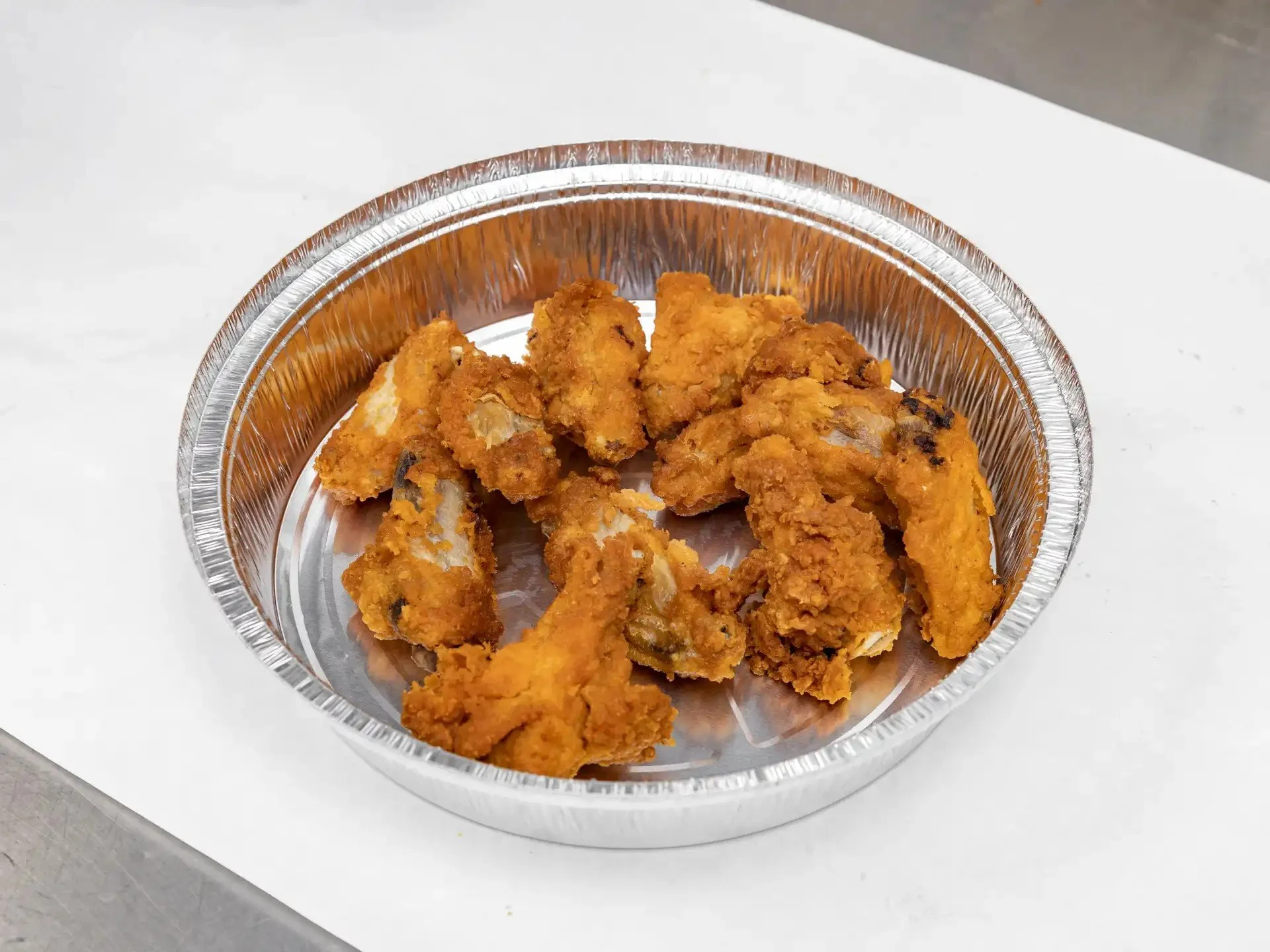 Fried chicken strips in a round aluminum tray on a white surface.
