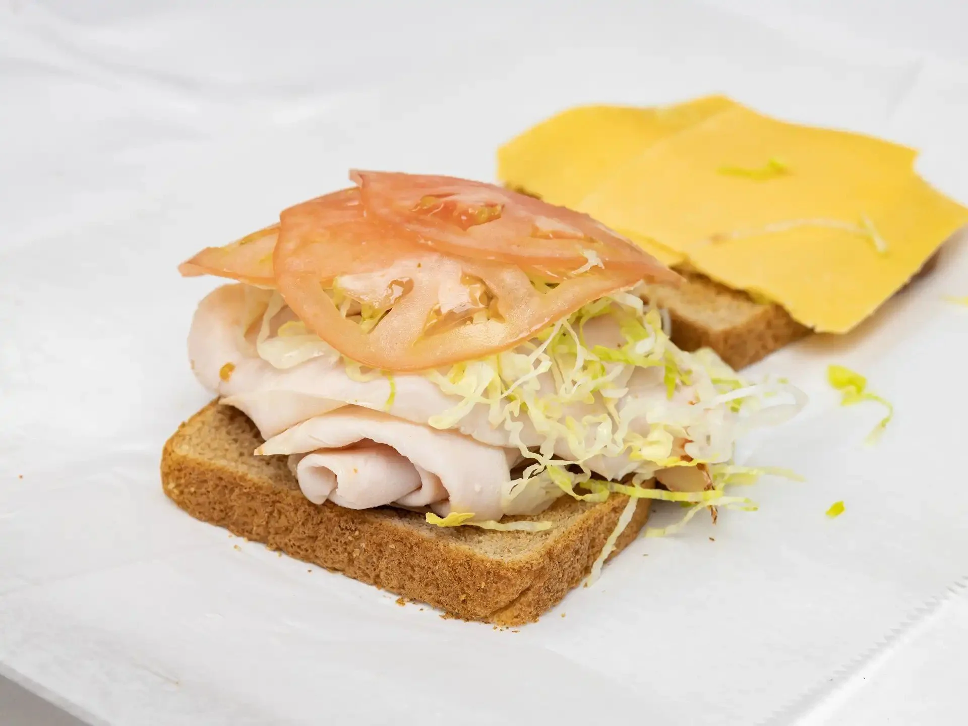 Open-faced sandwich with turkey, shredded lettuce, tomato slices, and cheddar cheese on whole wheat bread.