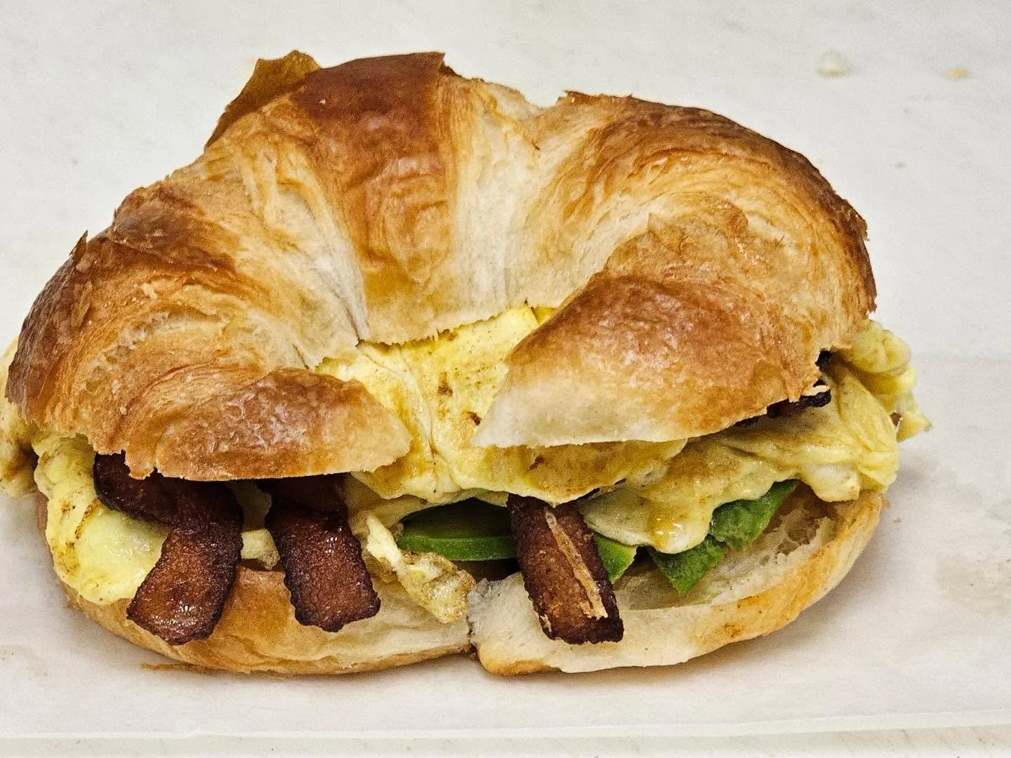 Breakfast sandwich with bacon, scrambled eggs, and green peppers in a croissant.