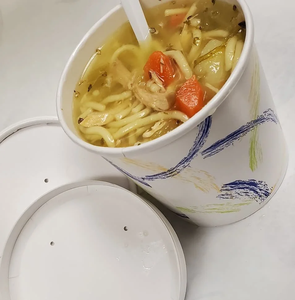 Cup of chicken noodle soup with vegetables on a disposable tray