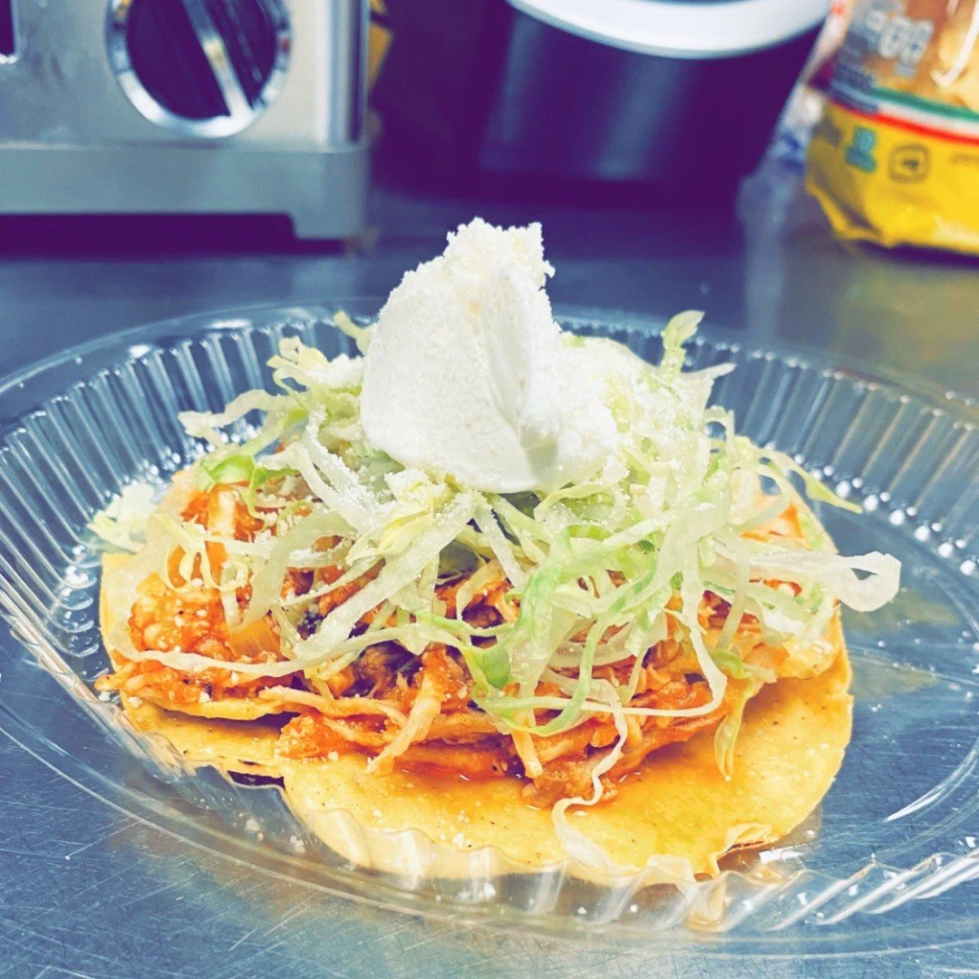 An open taco with shredded lettuce, meat, cheese, and a dollop of sour cream in a clear plastic container.