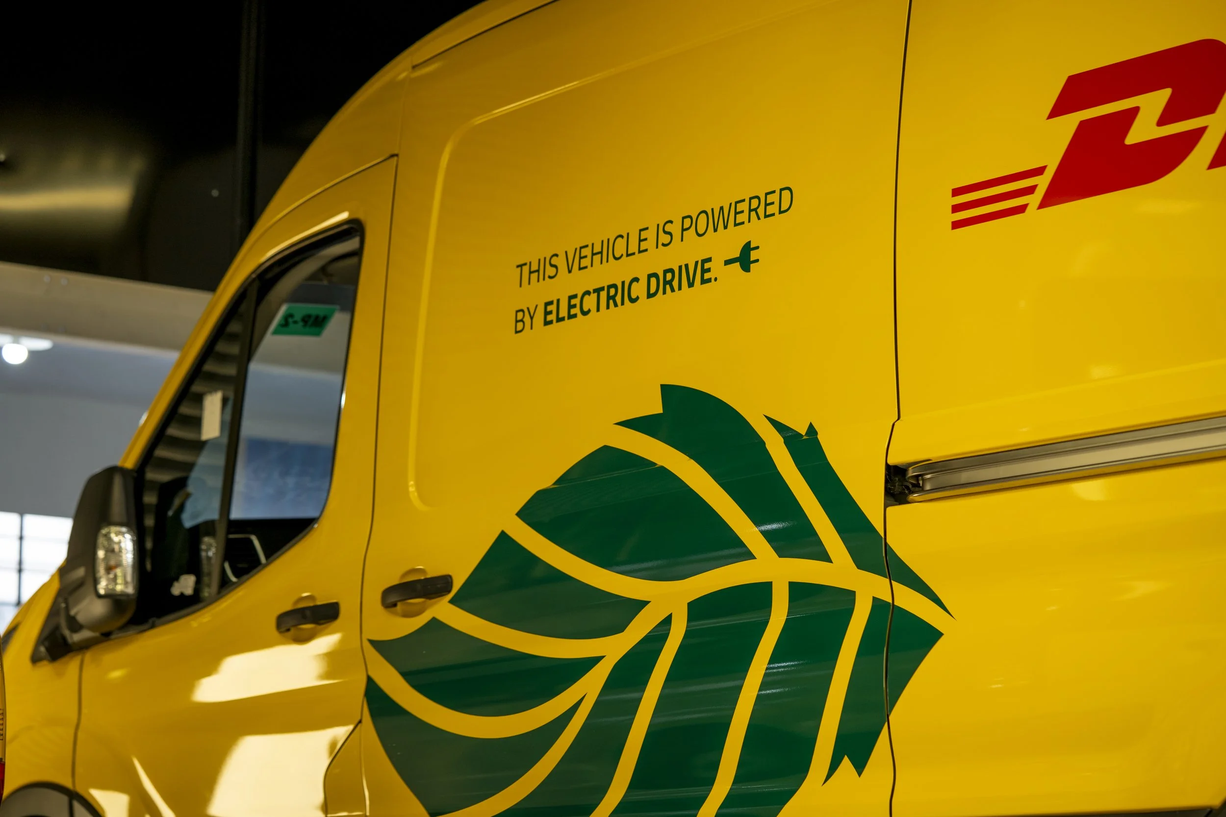 Yellow DHL delivery vehicle with green and red branding and text indicating it is powered by electric drive.