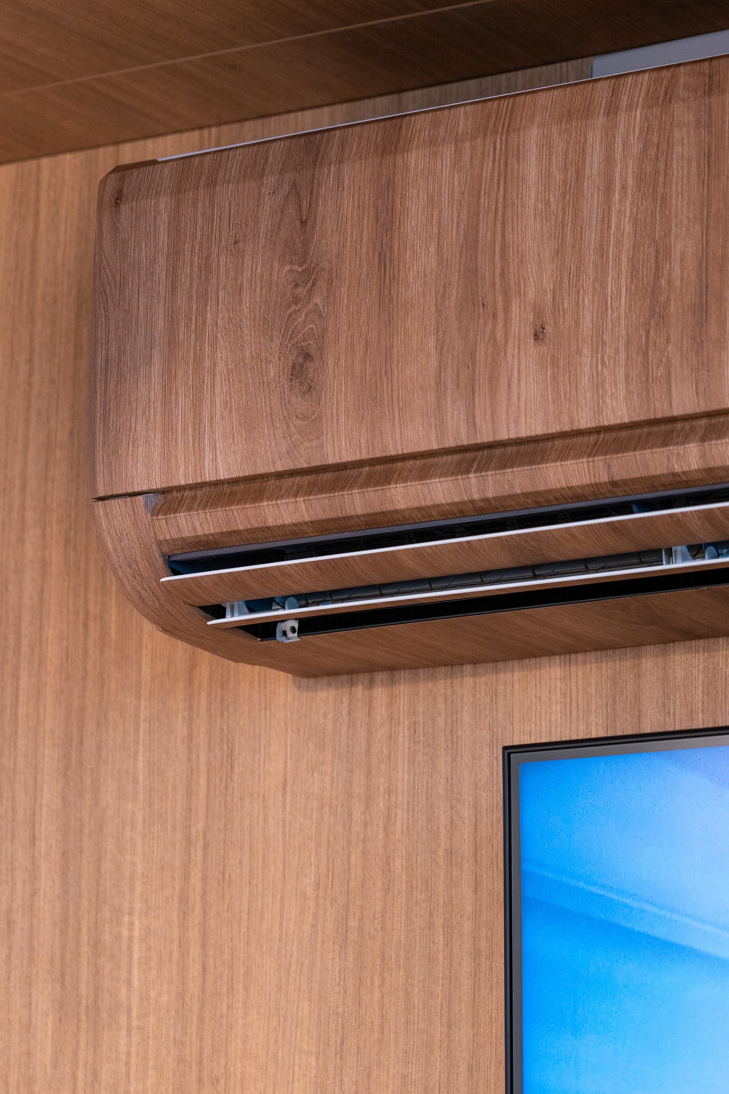 A wooden-colored air conditioning unit mounted on a wooden wall, showing the vents at the bottom.