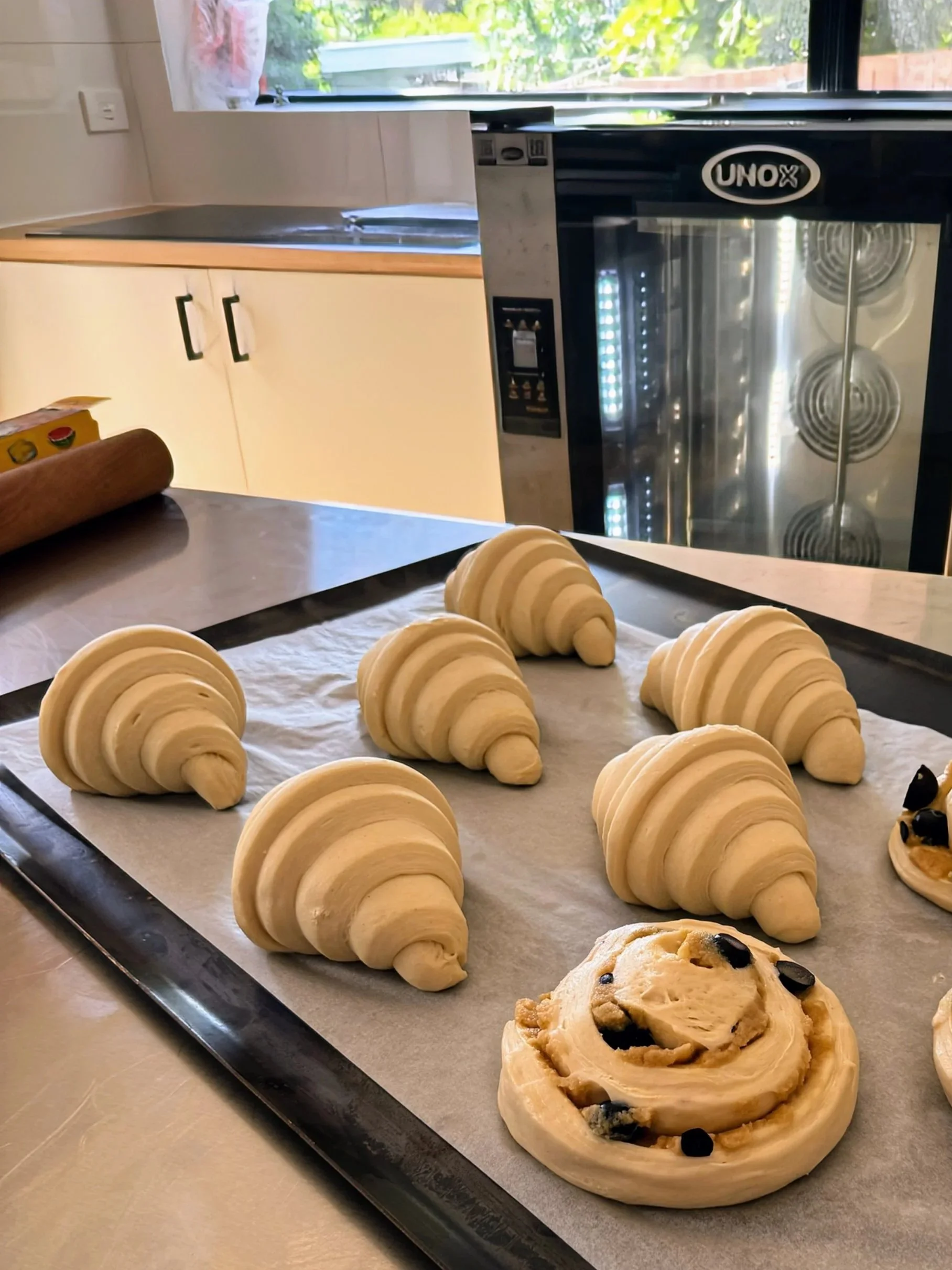 Unbaked croissant and pastry dough on a baking sheet lined with parchment paper in a kitchen.