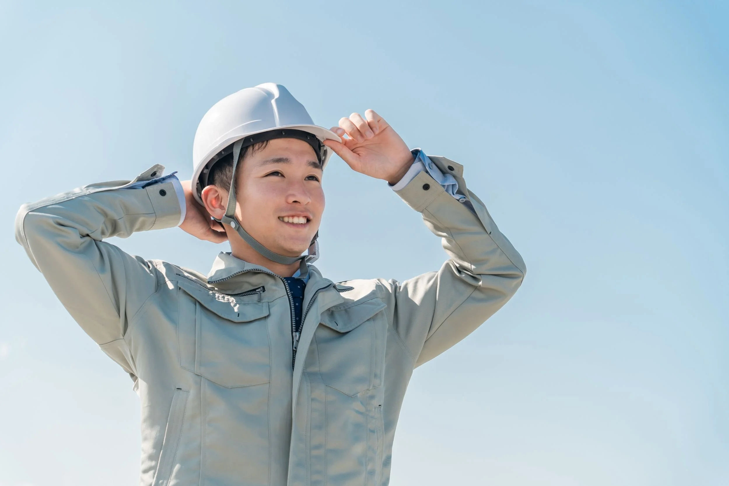 白いヘルメットを被り作業服を着た建設業の男性が笑顔で空を見上げている
