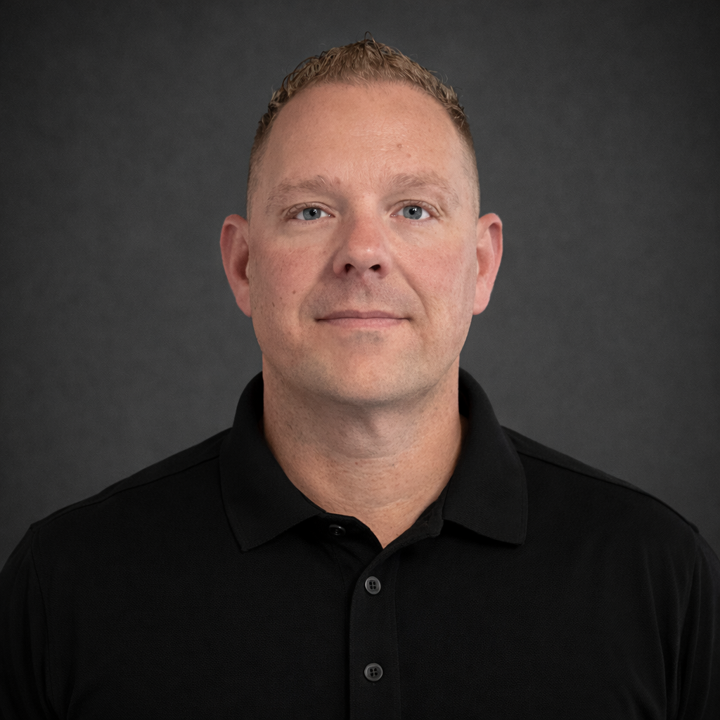 Portrait of a man with short reddish hair, blue eyes, wearing a black polo shirt, against a dark gray background.
