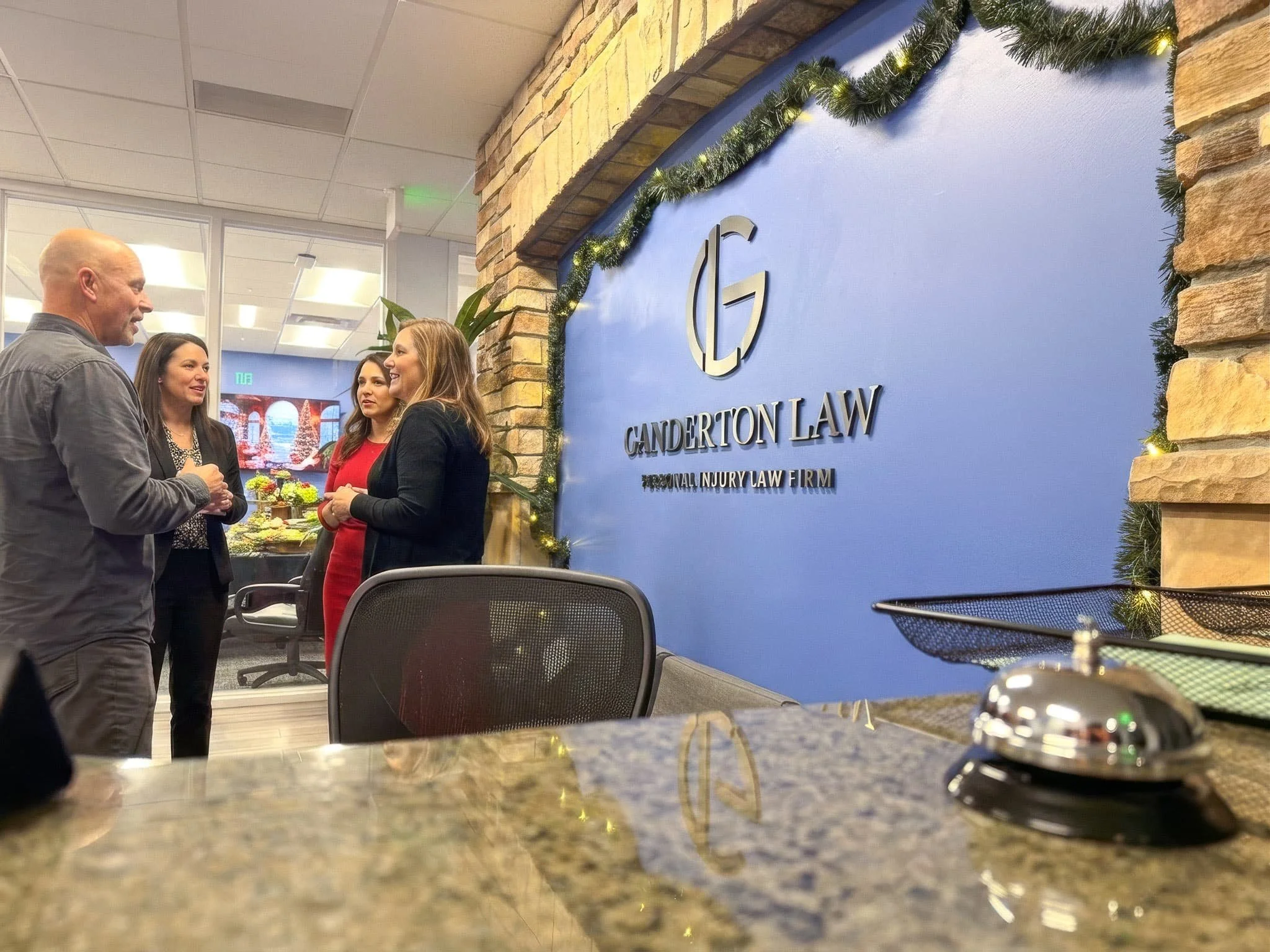 Four people standing together and talking in an office or lobby decorated with holiday garlands and a branded sign for Canderton Law.