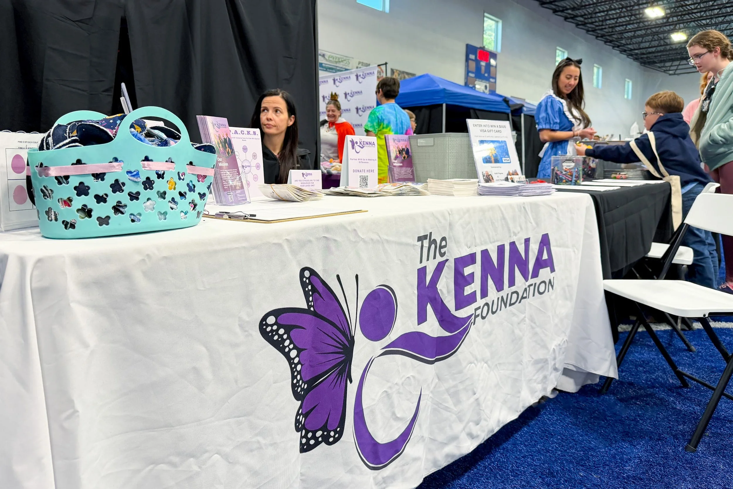 A table at an event with promotional materials and donations for the Kenna Foundation, featuring a large butterfly logo on a purple banner.