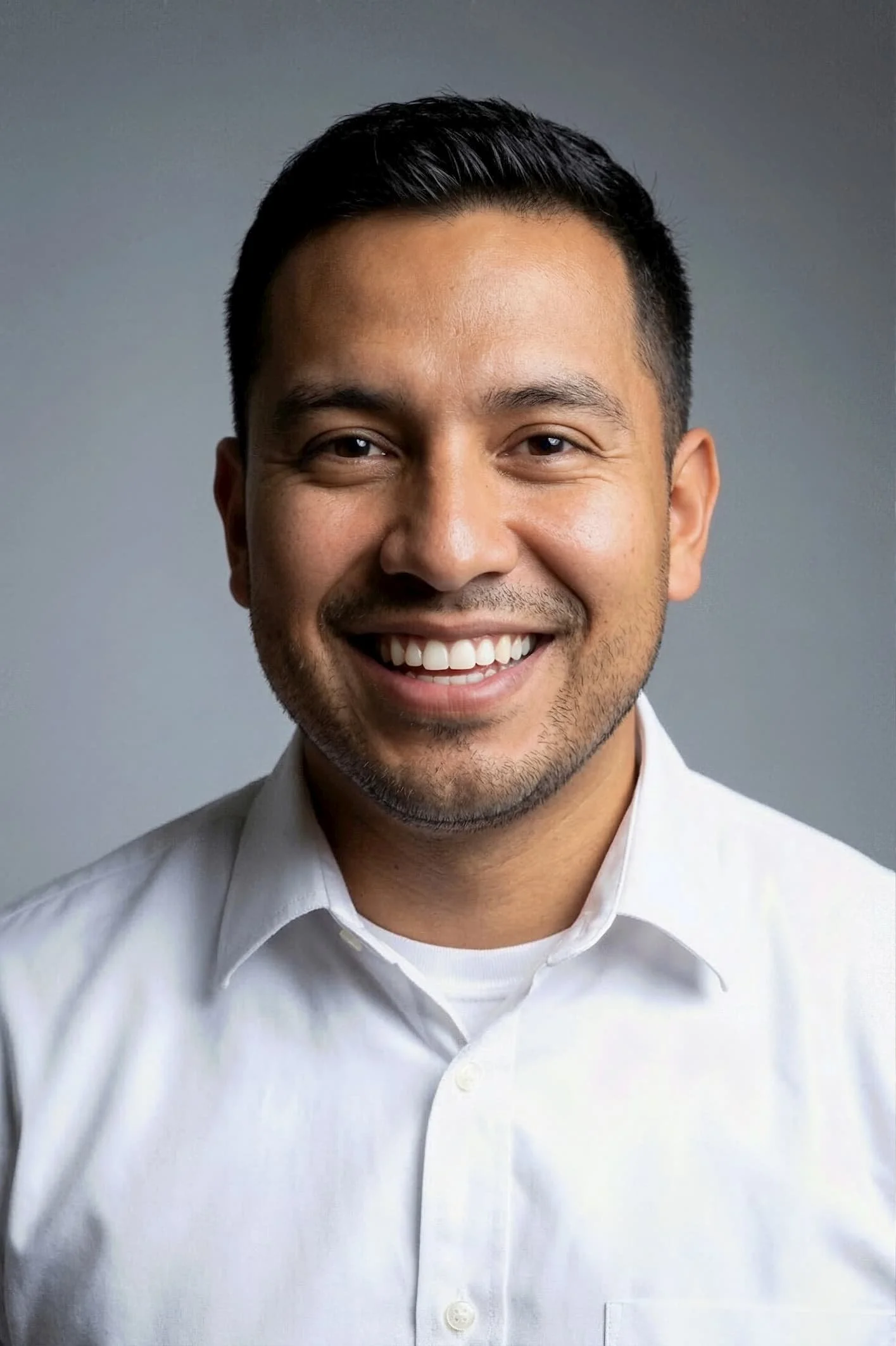 Close-up of a smiling man with black hair, wearing a white button-up shirt against a gray background.