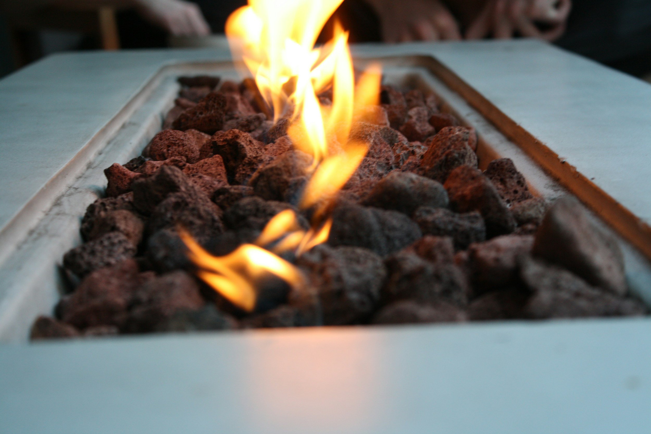 Close-up of a gas fireplace with orange flames rising from dark volcanic rocks on a white surface.