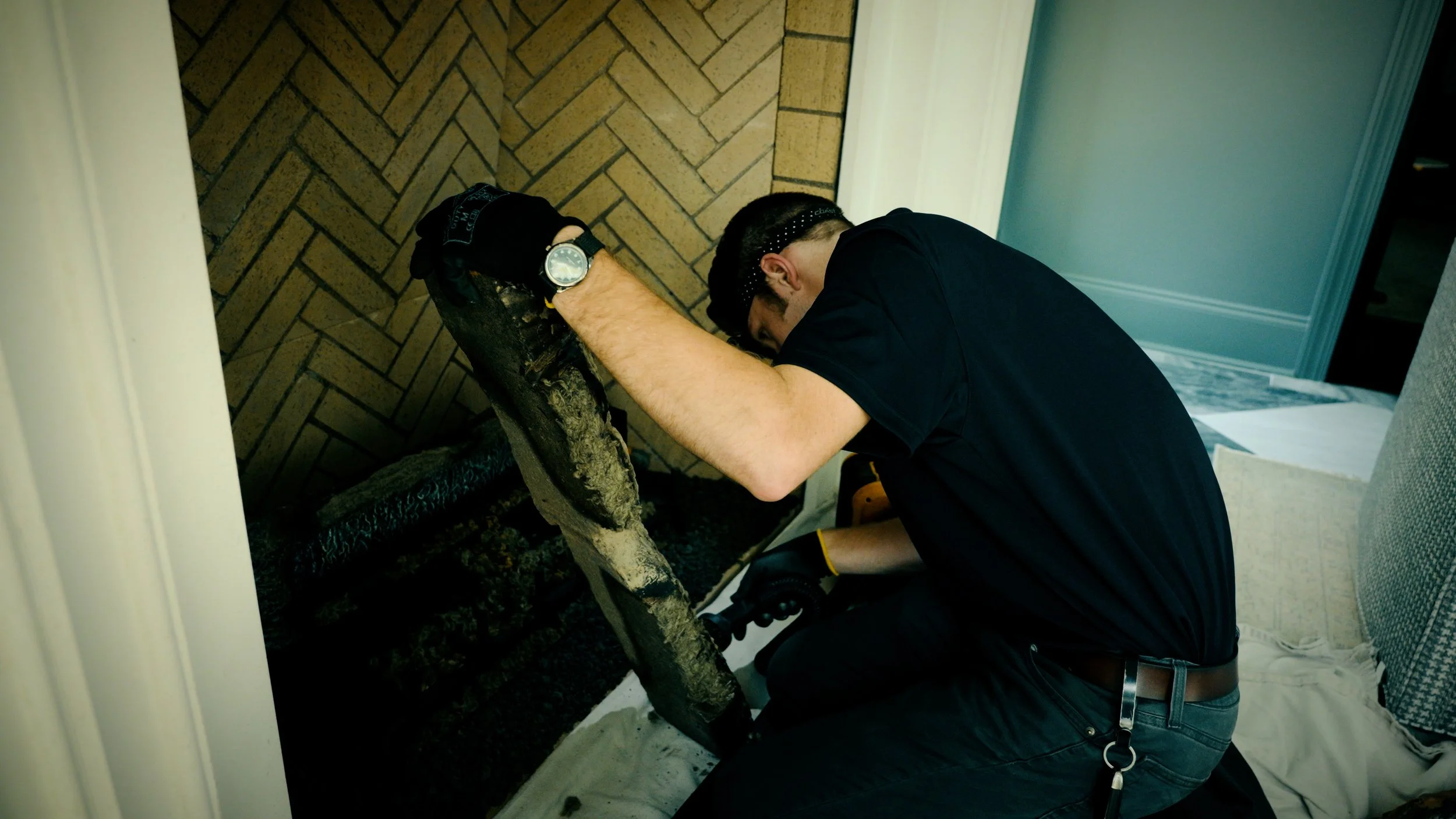 A man working on a fireplace, possibly performing maintenance or repairing, with a gas log and tools around him.