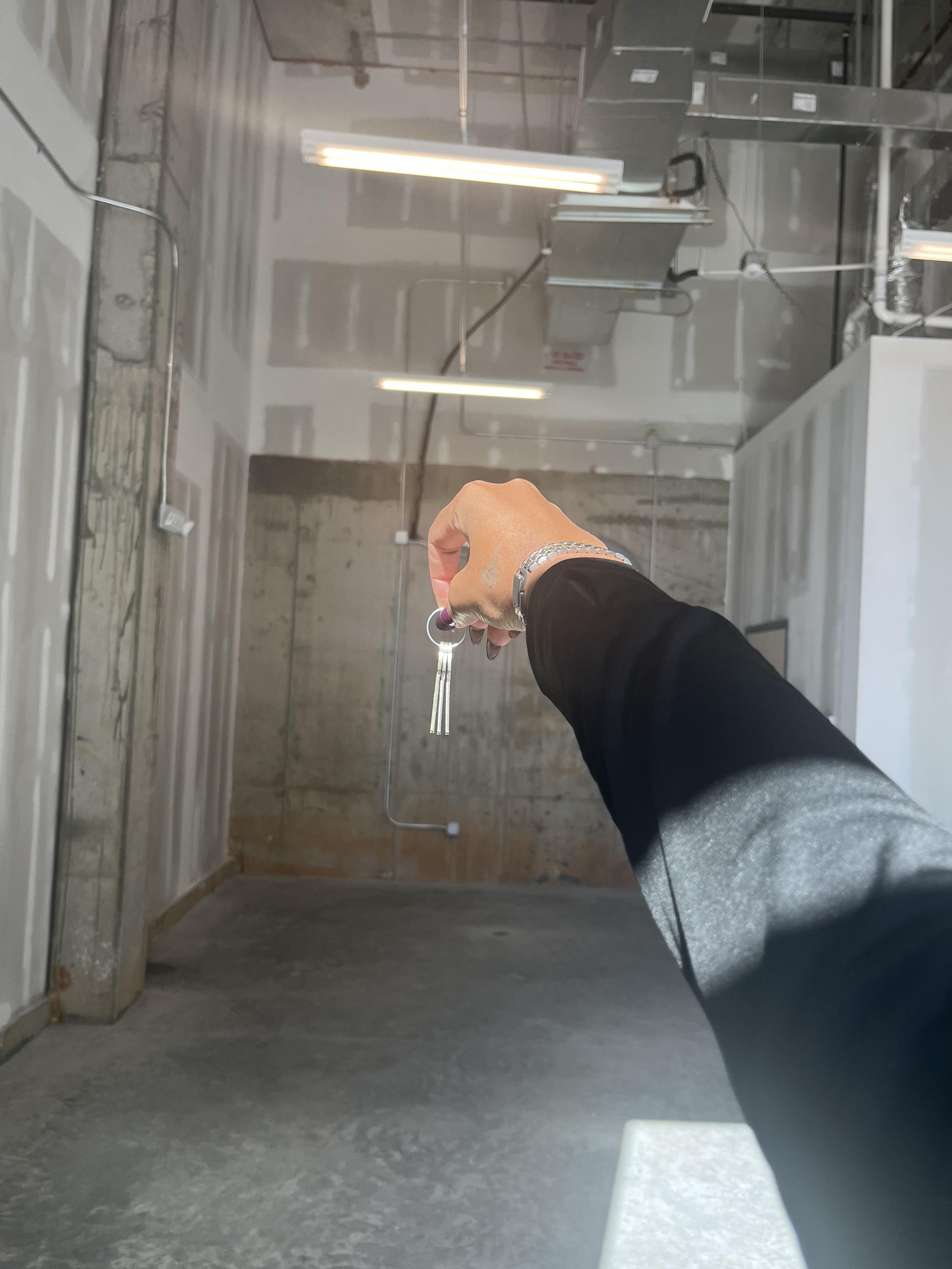 Person holding keys in an industrial-looking space with unfinished walls and ceiling fixtures.