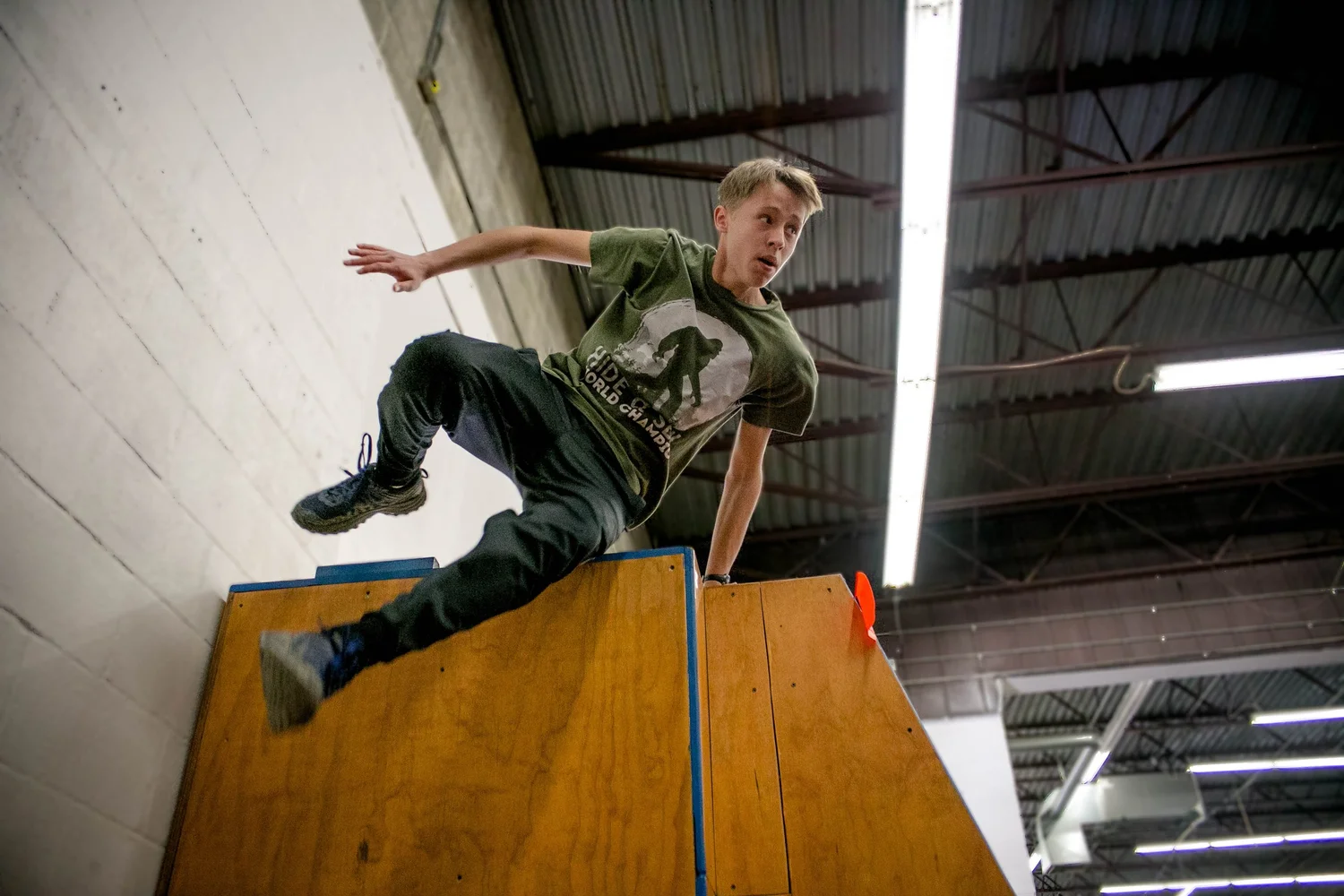 A teen parkour student performing a vault over a wooden obstacle