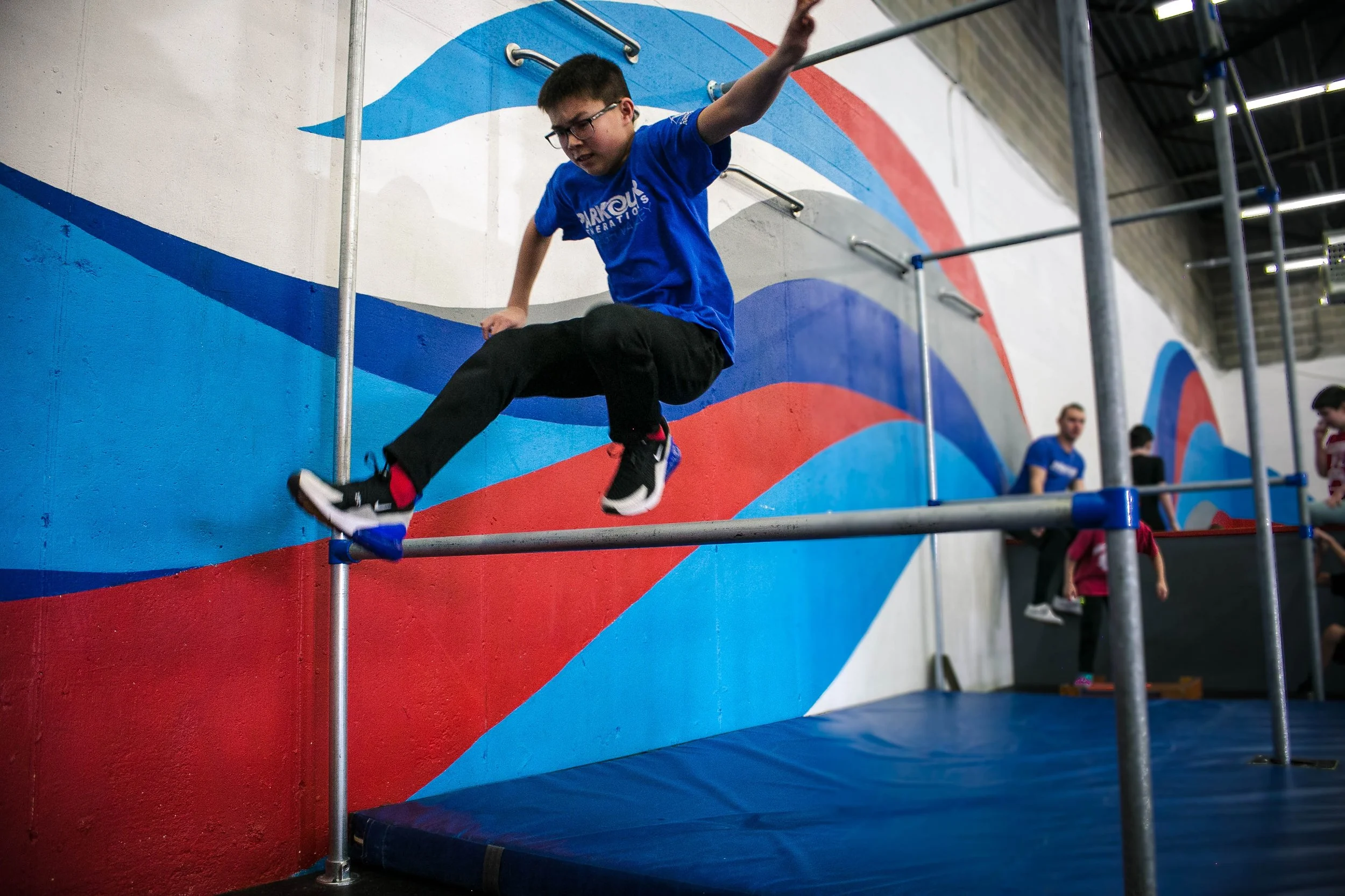 A youth parkour student in a blue shirt practicing a controlled rail movement