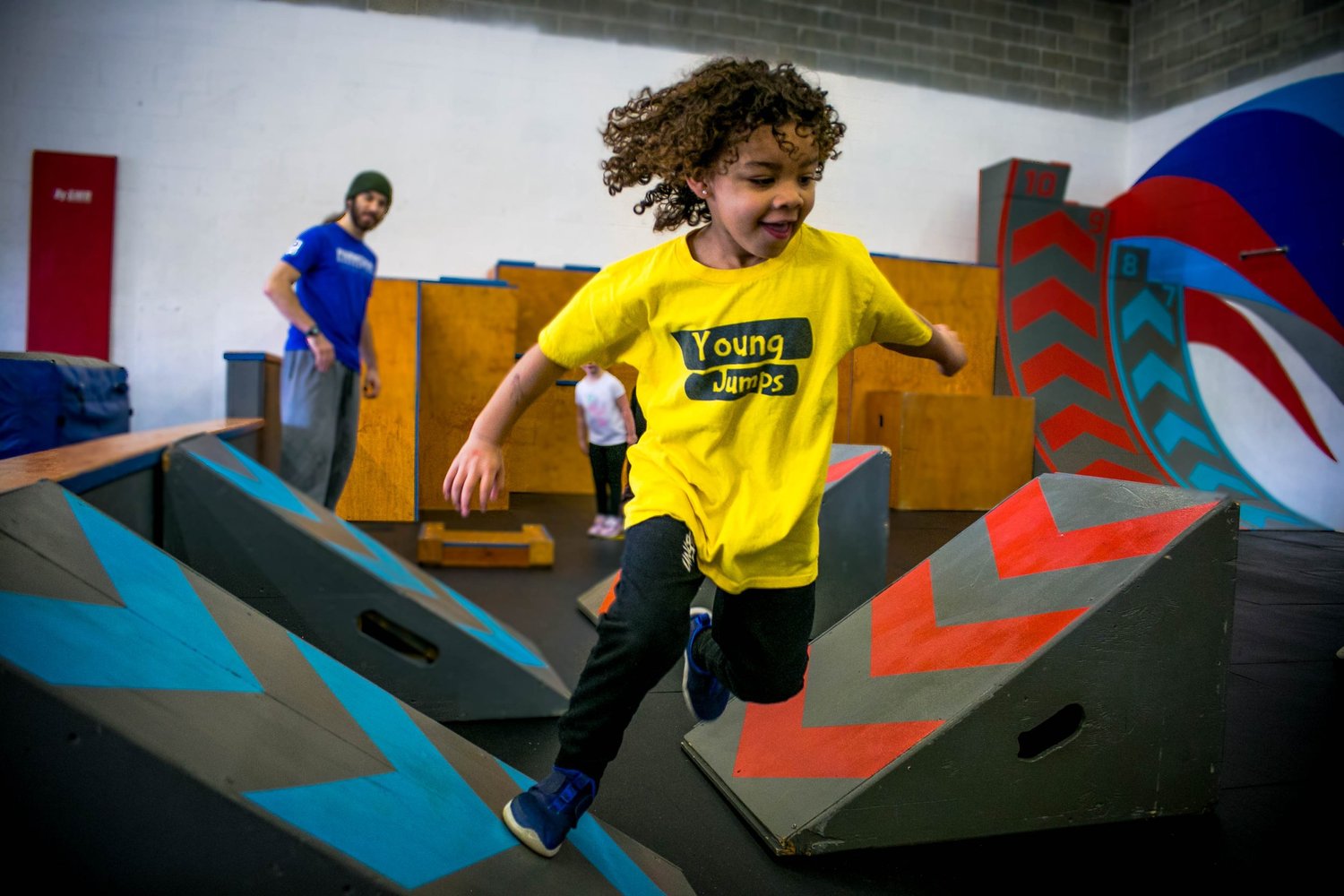 A preschool-age parkour student in a yellow Mini program shirt moving through an obstacle course