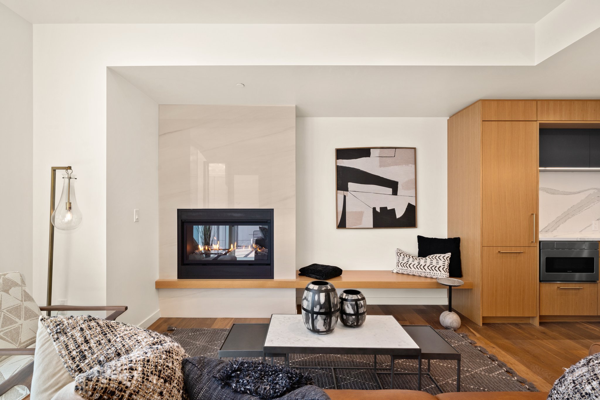 Living room with modern decor including a fireplace, abstract wall art, a sofa with patterned cushions, a coffee table with decorative vases, and a wooden cabinet.