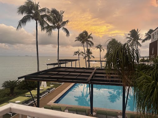 Beachside hotel pool area at sunset with palm trees, lounge chairs, and a view of the ocean