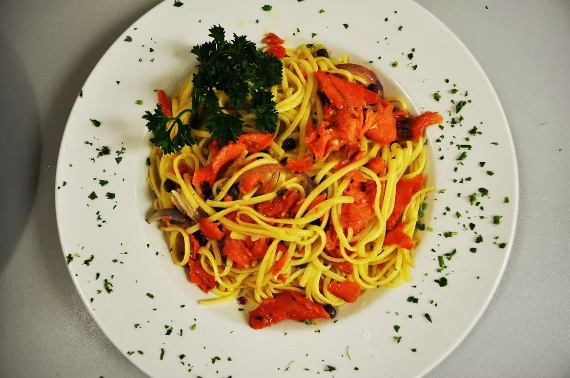 Plate of spaghetti pasta with tomato sauce, garnished with parsley and herbs.