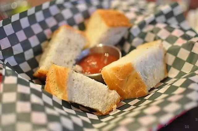 Pieces of bread surrounding a small dish of marinara sauce in a basket with black and white checkered paper