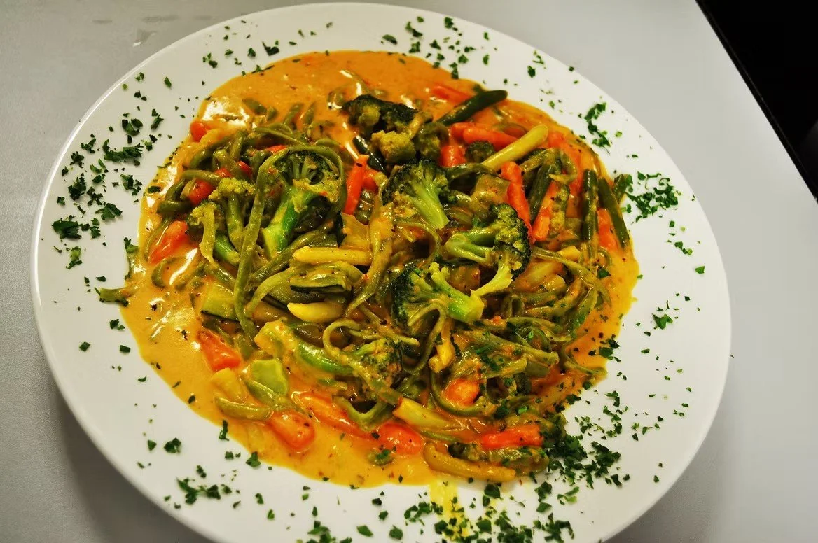 Plate of vegetable curry with broccoli, carrots, and green beans garnished with chopped parsley.