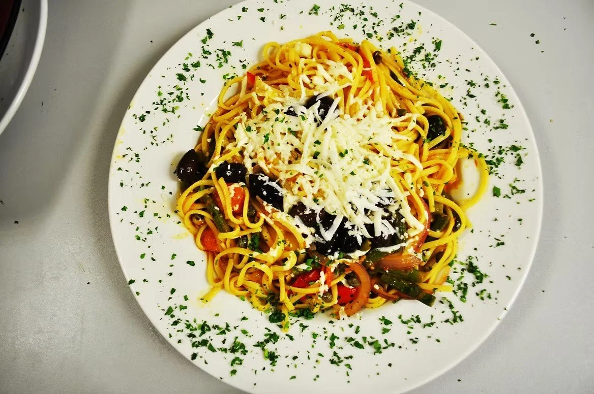 Plate of spaghetti with black olives, cherry tomatoes, grated cheese, and chopped parsley.